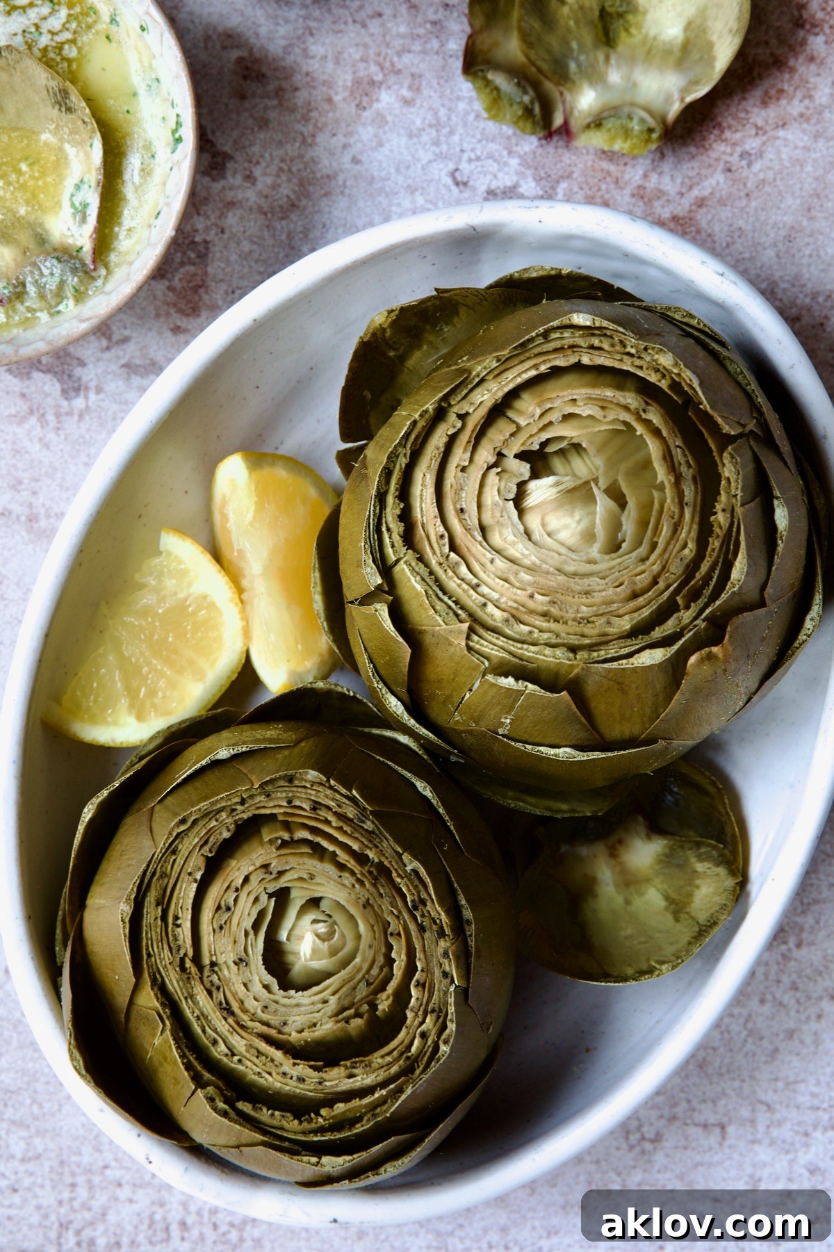 Two tender Instant Pot Artichokes served in a white oval bowl, garnished with fresh lemon wedges, showcasing the inviting garlic butter sauce.