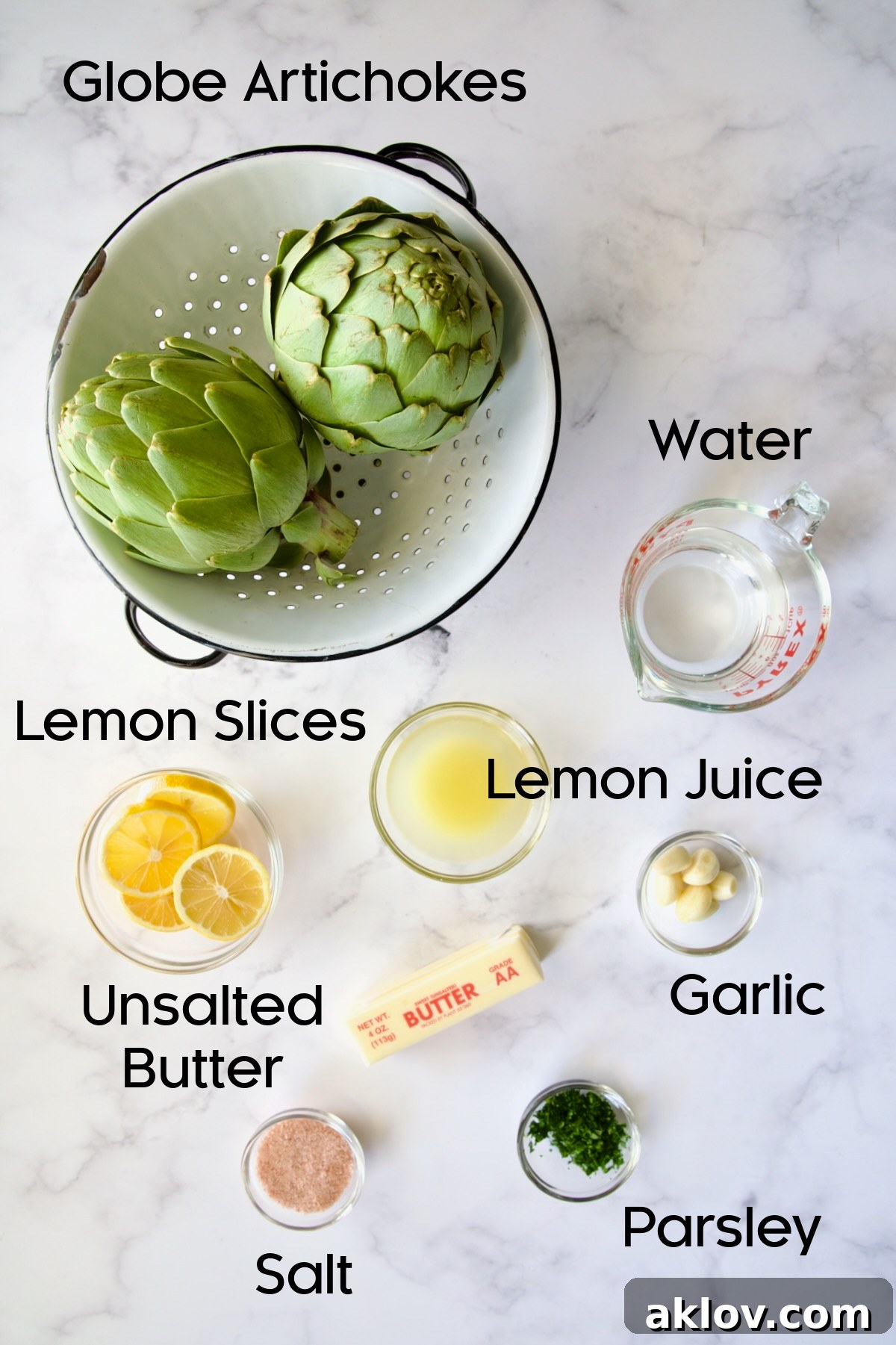 Fresh ingredients for Instant Pot Artichokes, including globe artichokes, lemons, garlic, butter, and parsley, arranged on a countertop.