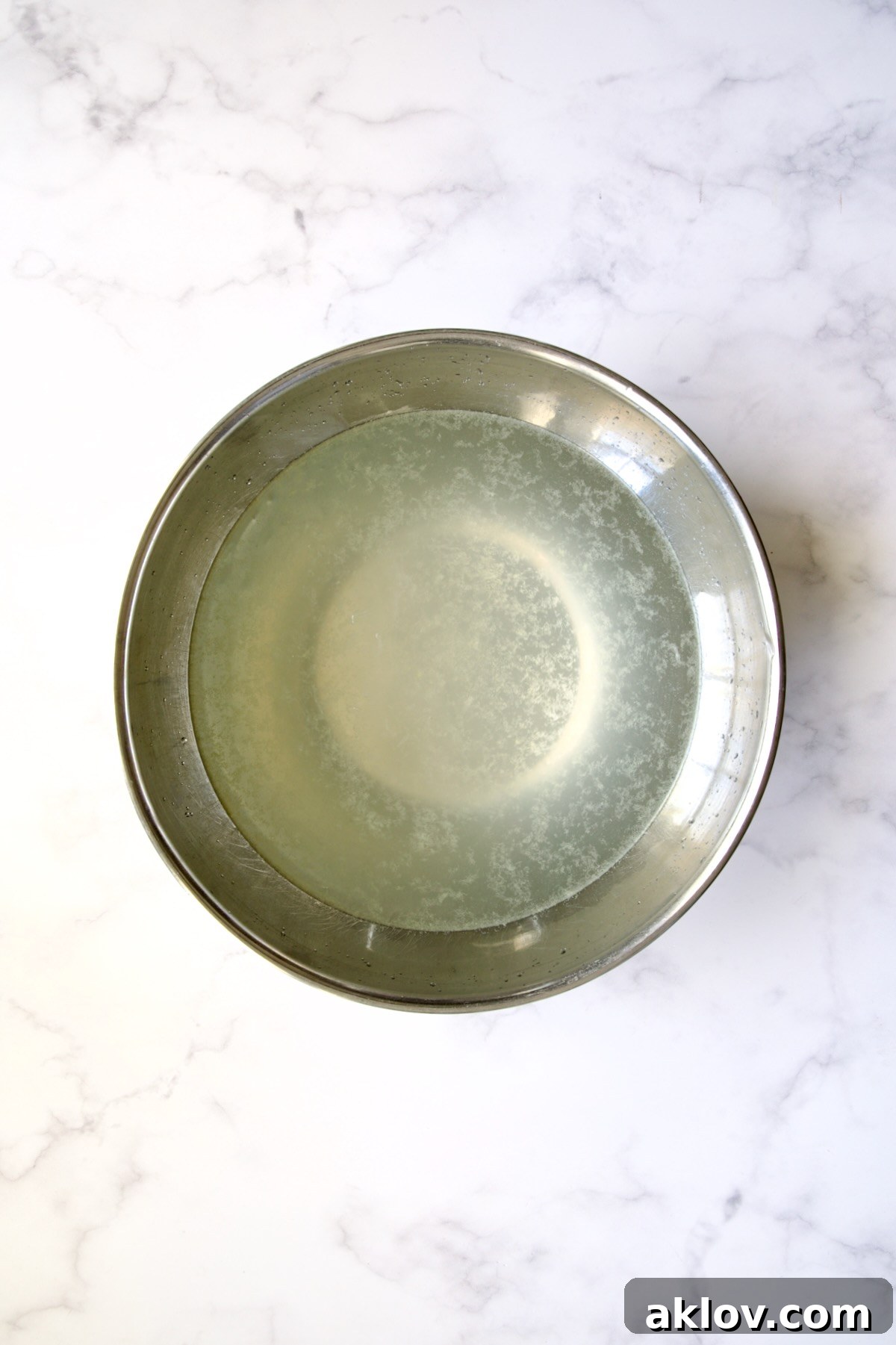 Stainless steel bowl filled with lemon water, ready for artichoke preparation.