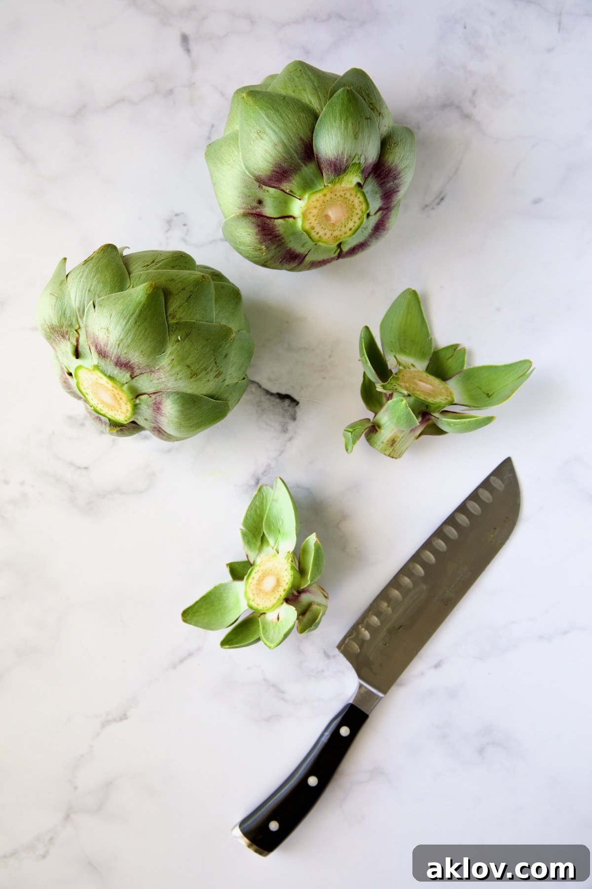Two globe artichokes with their stems neatly trimmed using a chef's knife, ready for further preparation.