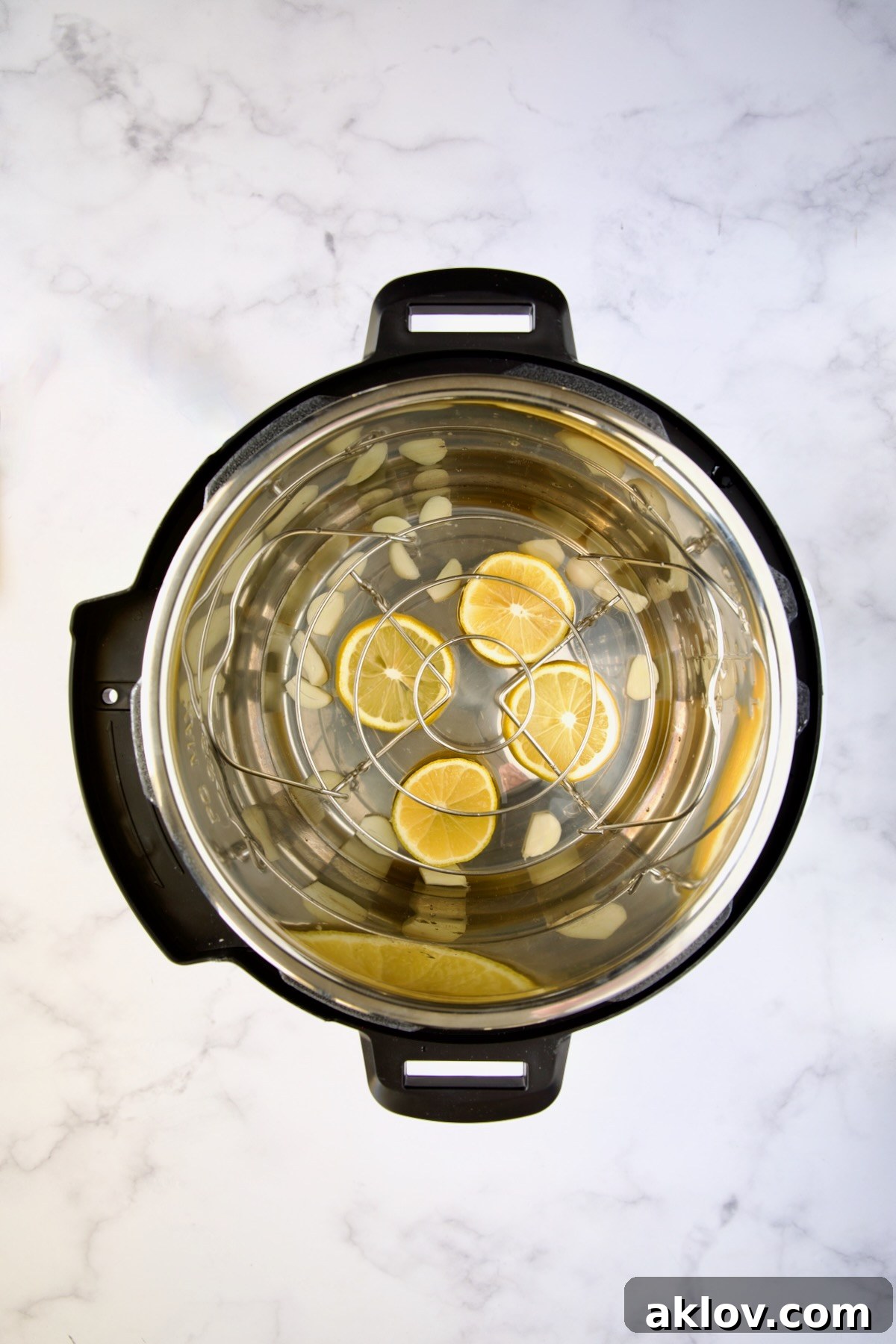 Lemon slices and garlic cloves arranged at the bottom of an Instant Pot, providing aromatic steam for the artichokes.