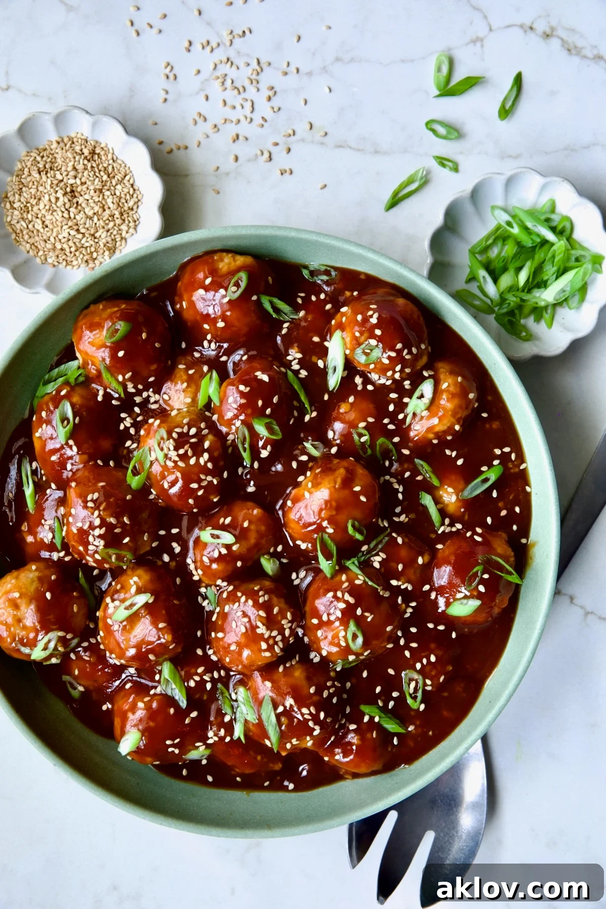 Asian Chicken Meatballs in a round green bowl, garnished with sesame seeds and chopped scallions.