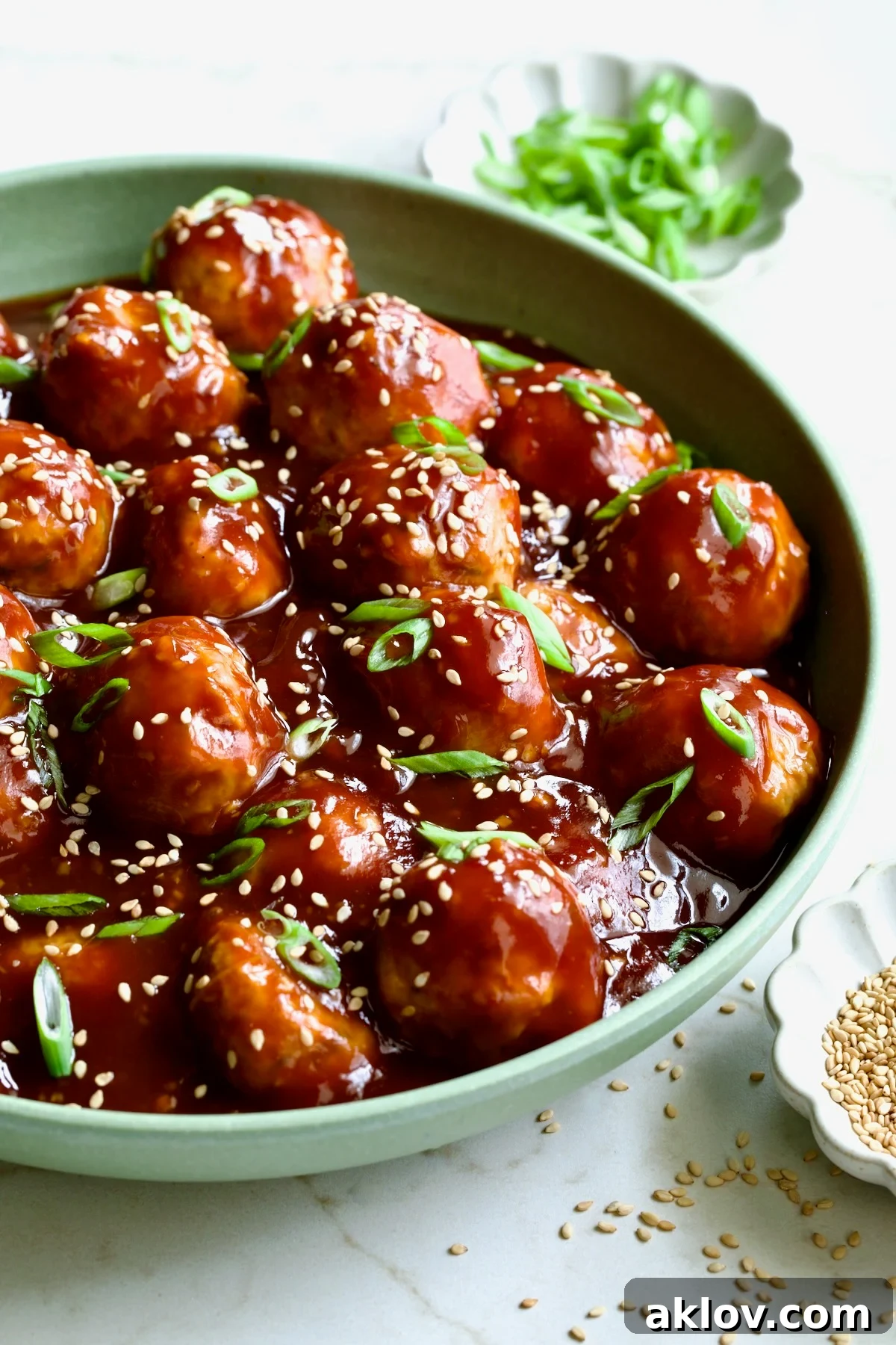Close-up of Asian Chicken Meatballs in a round green bowl, garnished with sesame seeds and scallions.