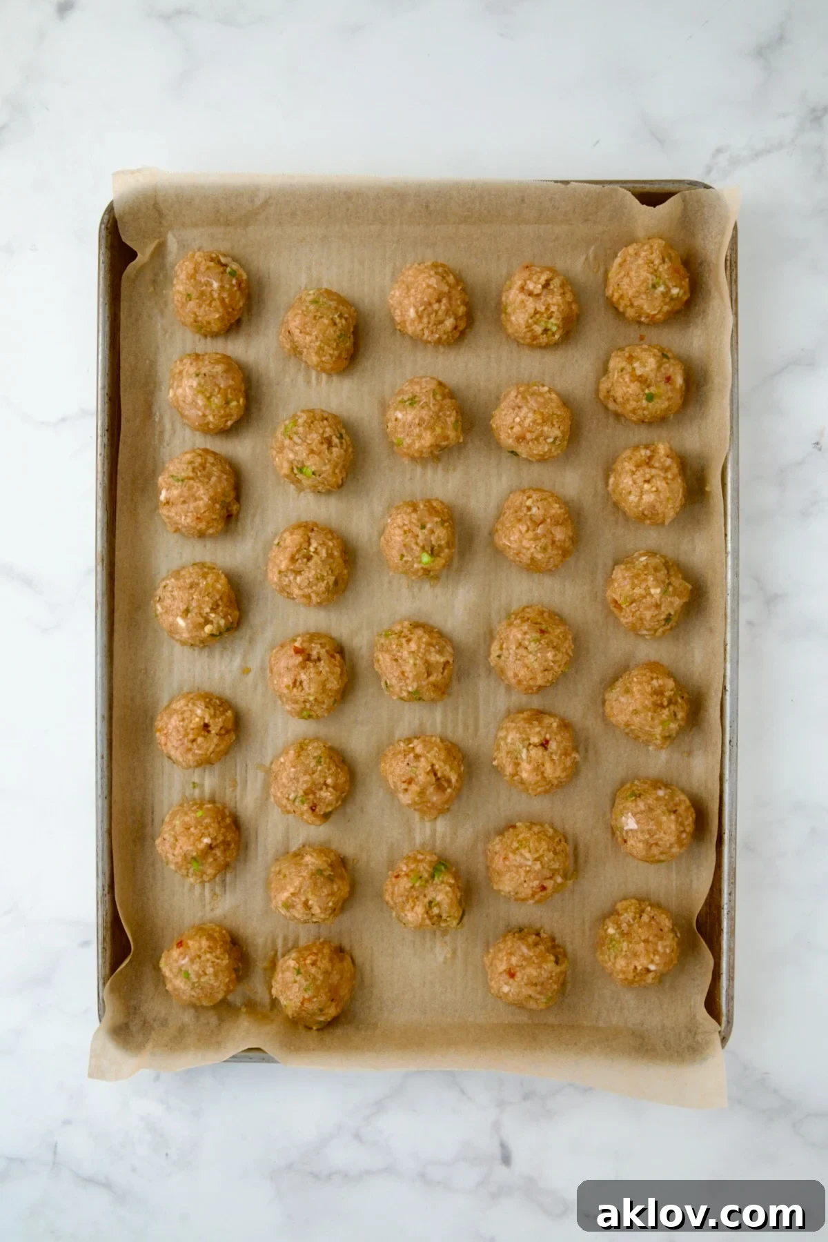 Uncooked chicken meatballs neatly arranged on a parchment paper-lined baking sheet.