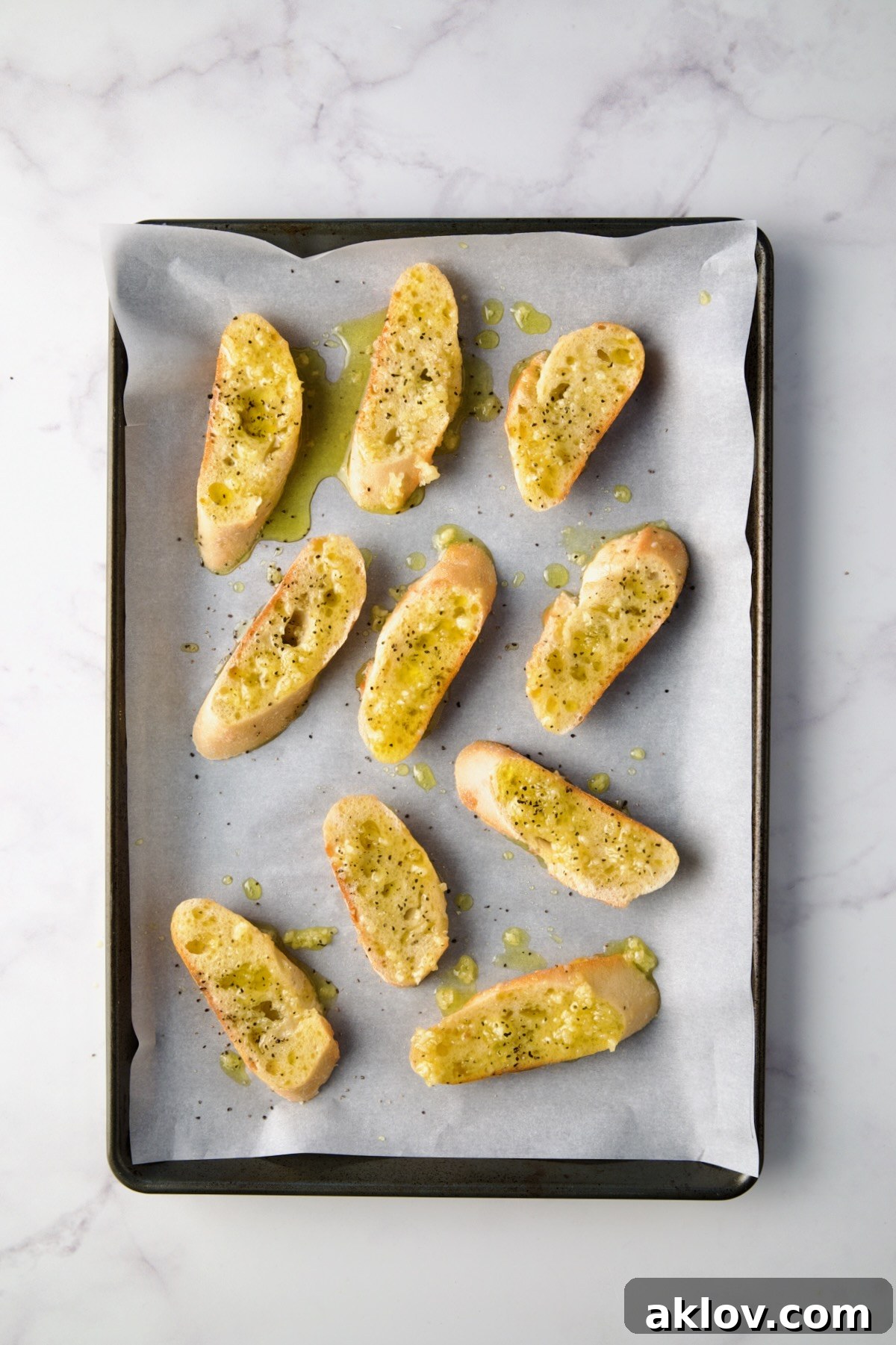 Baguette slices on a baking sheet, brushed with a fragrant mixture of olive oil and minced garlic, ready for seasoning and cheese.
