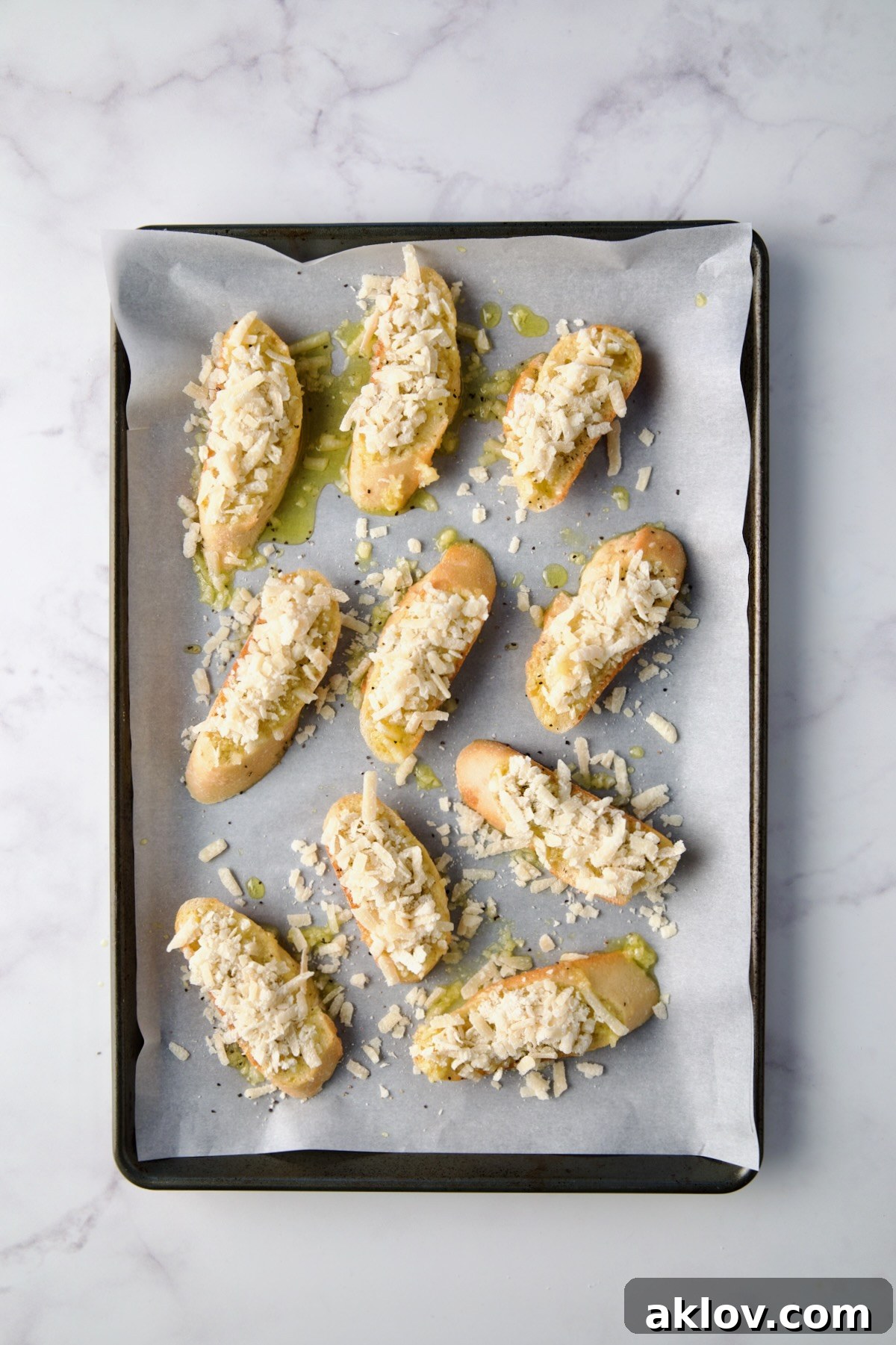 Bread slices on a baking sheet, generously topped with freshly grated Parmesan cheese.