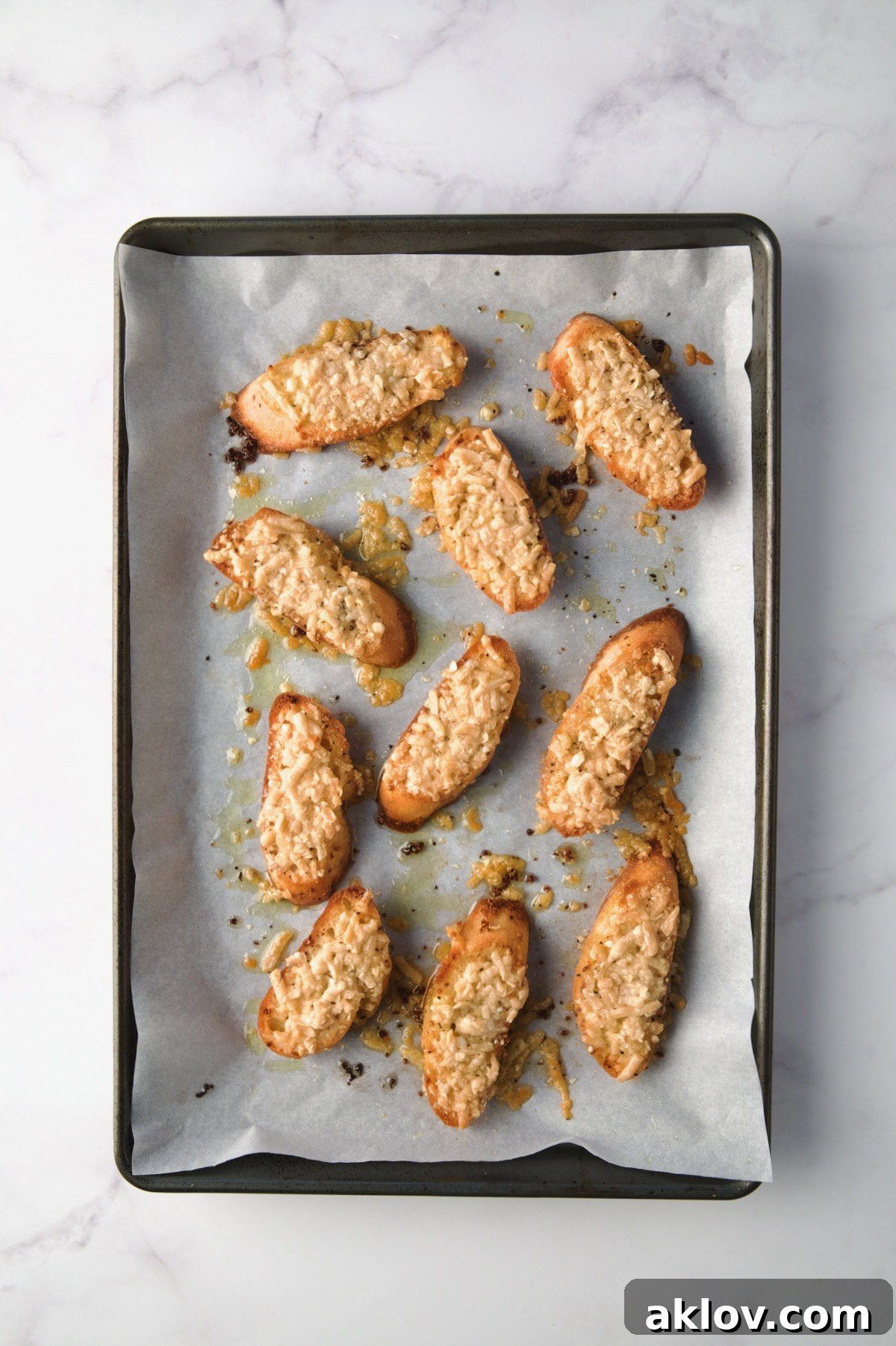 Golden-brown Parmesan toasts, with melted and slightly crisped cheese, are presented on a parchment paper-lined baking sheet, freshly baked and ready to serve.