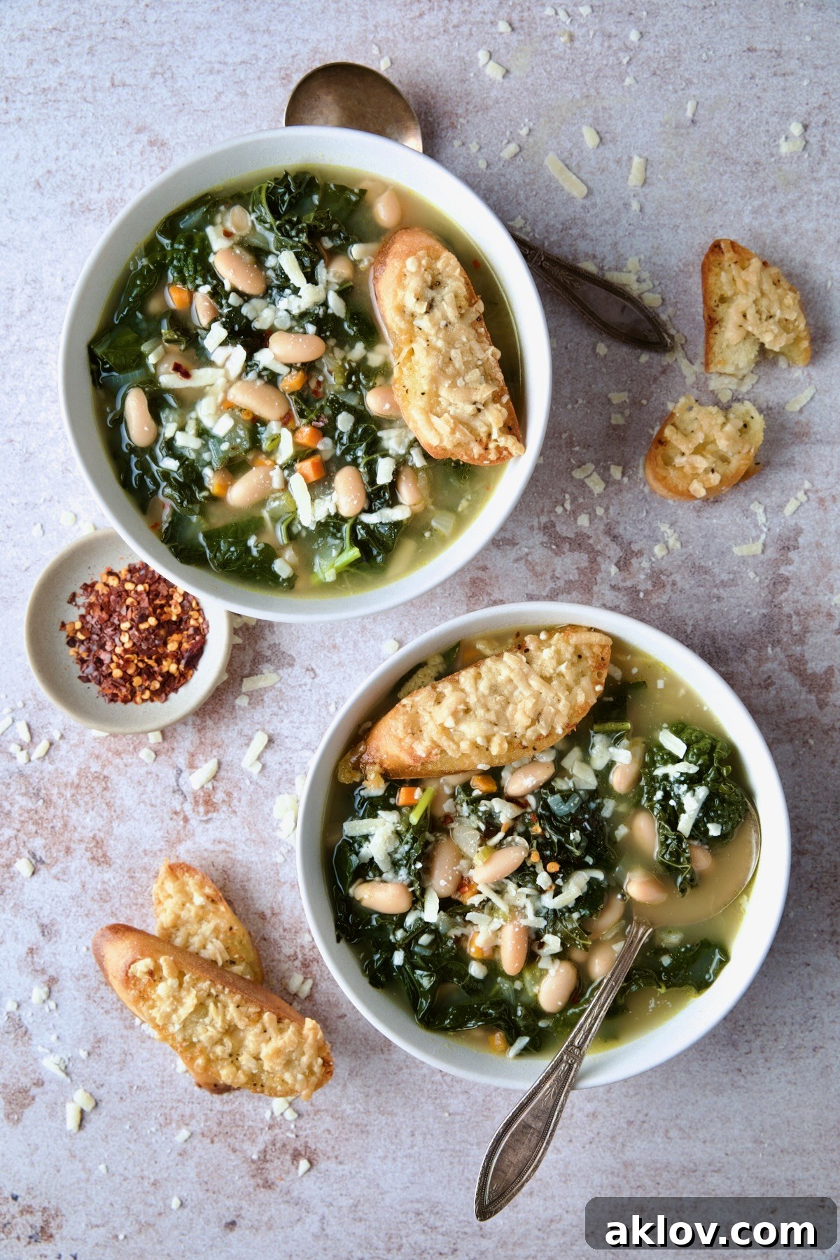 Two steaming bowls of homemade White Bean Kale Soup, garnished with fresh herbs and served with Parmesan Toast.