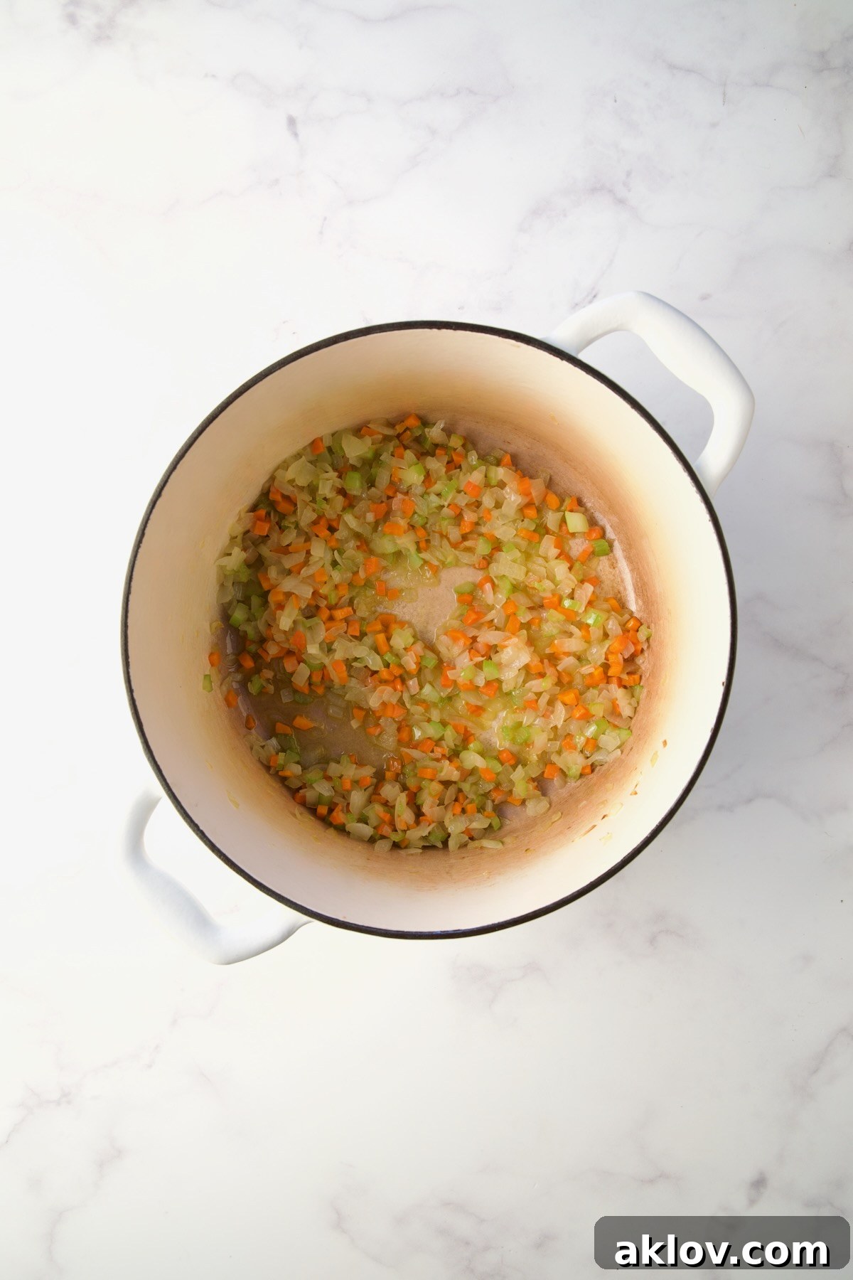Finely chopped onions, carrots, and celery gently cooking in olive oil in a white Dutch oven.