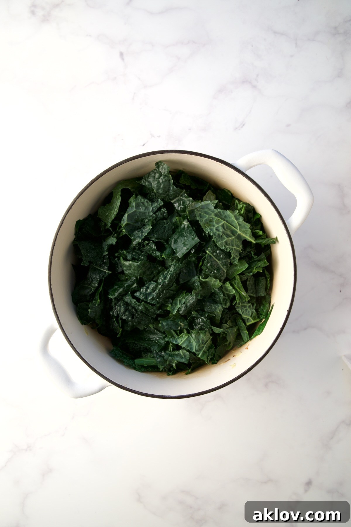 Fresh Lacinato kale leaves added to the simmering vegetable base in a Dutch oven, ready to wilt.