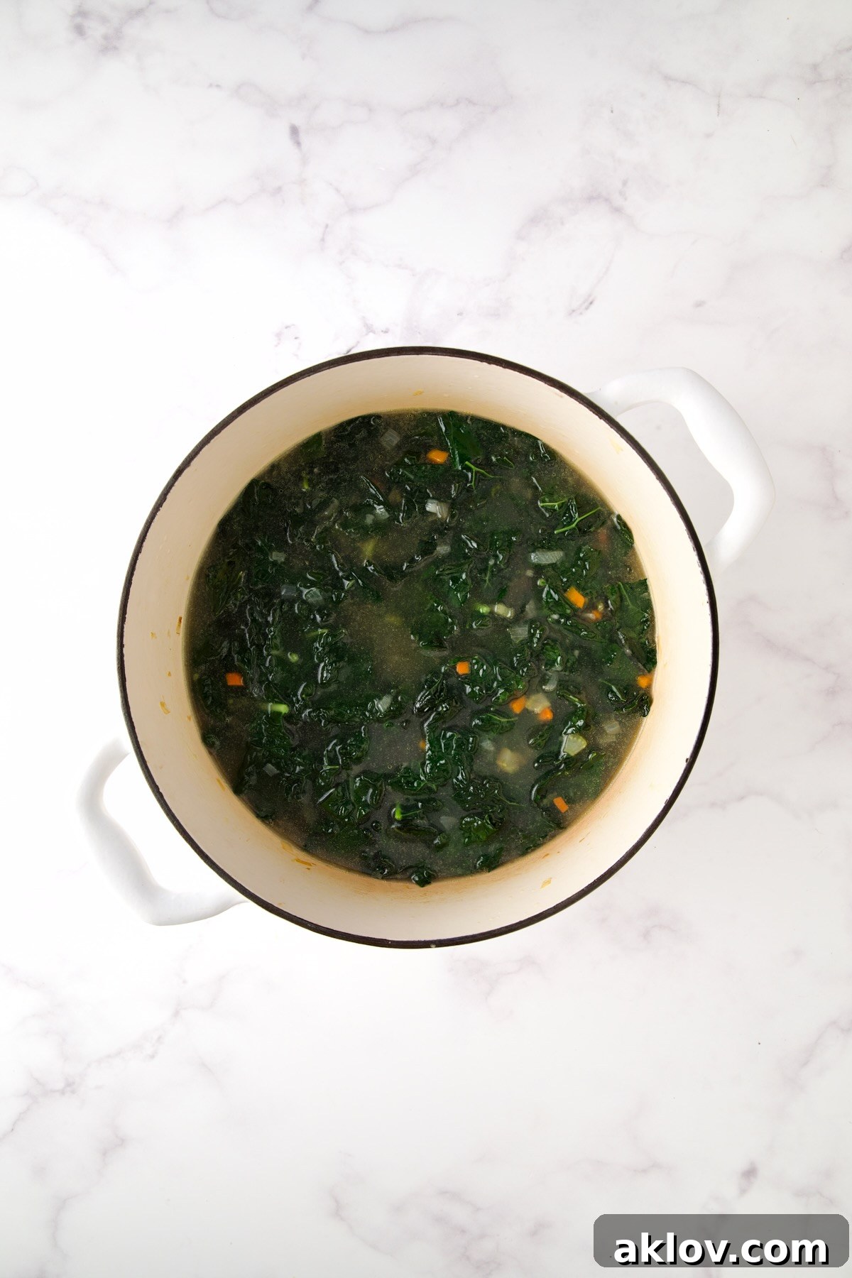 The sautéed vegetables and wilted kale are now covered with rich chicken broth in the Dutch oven, creating the liquid base for the soup.