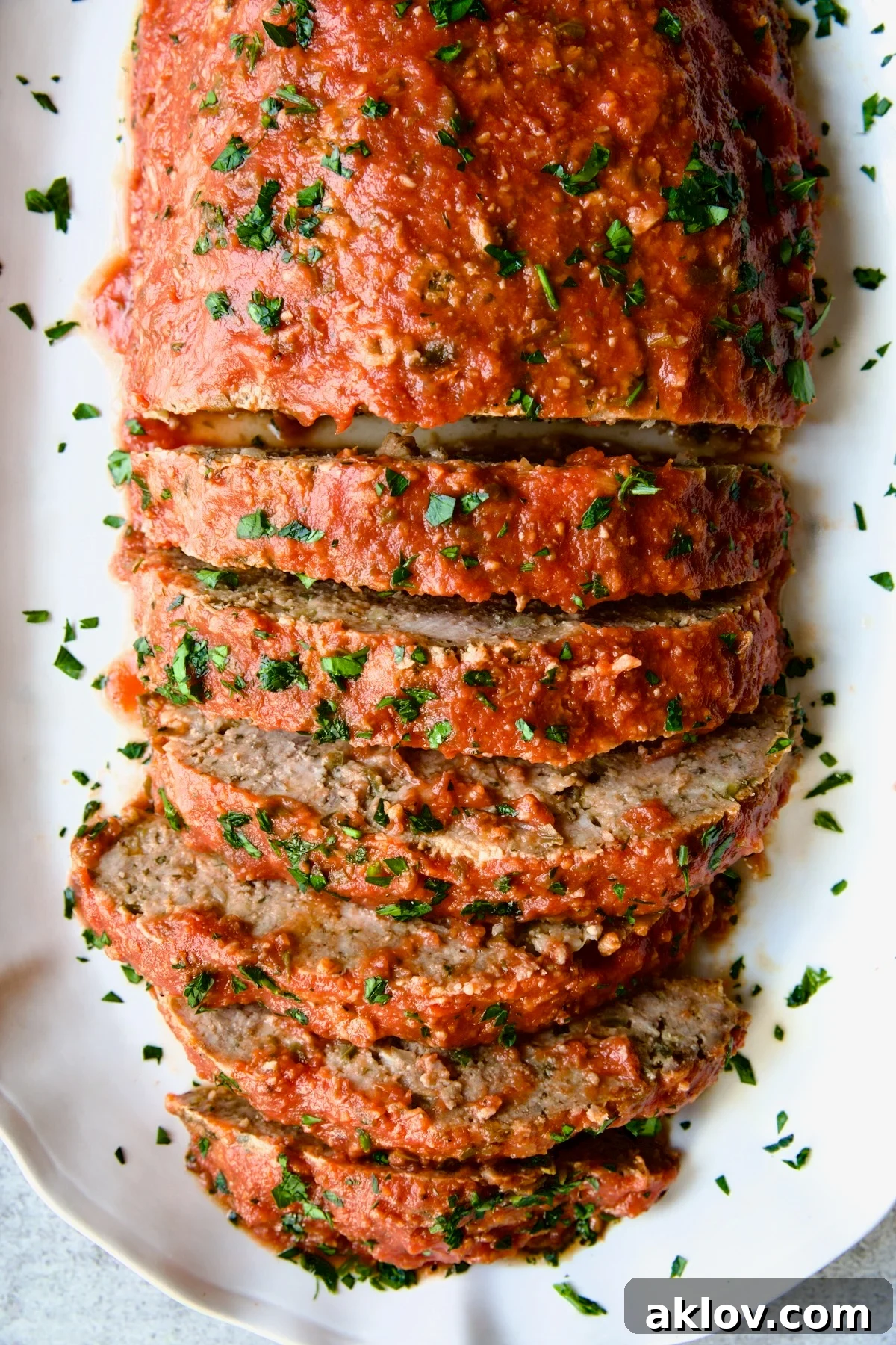 Sliced Italian Meatloaf on a white platter, garnished with fresh parsley.