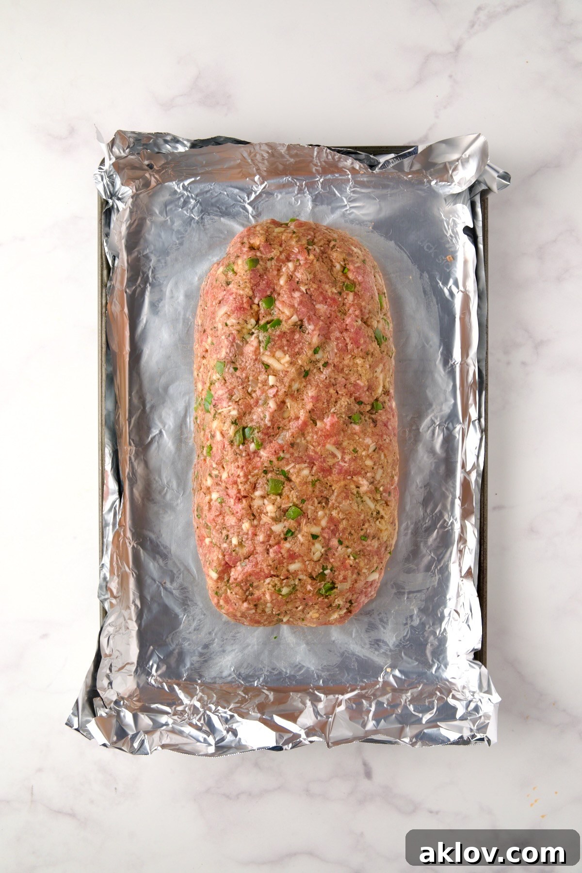 Meatloaf before being baked on an aluminum foil-lined rimmed sheet pan.