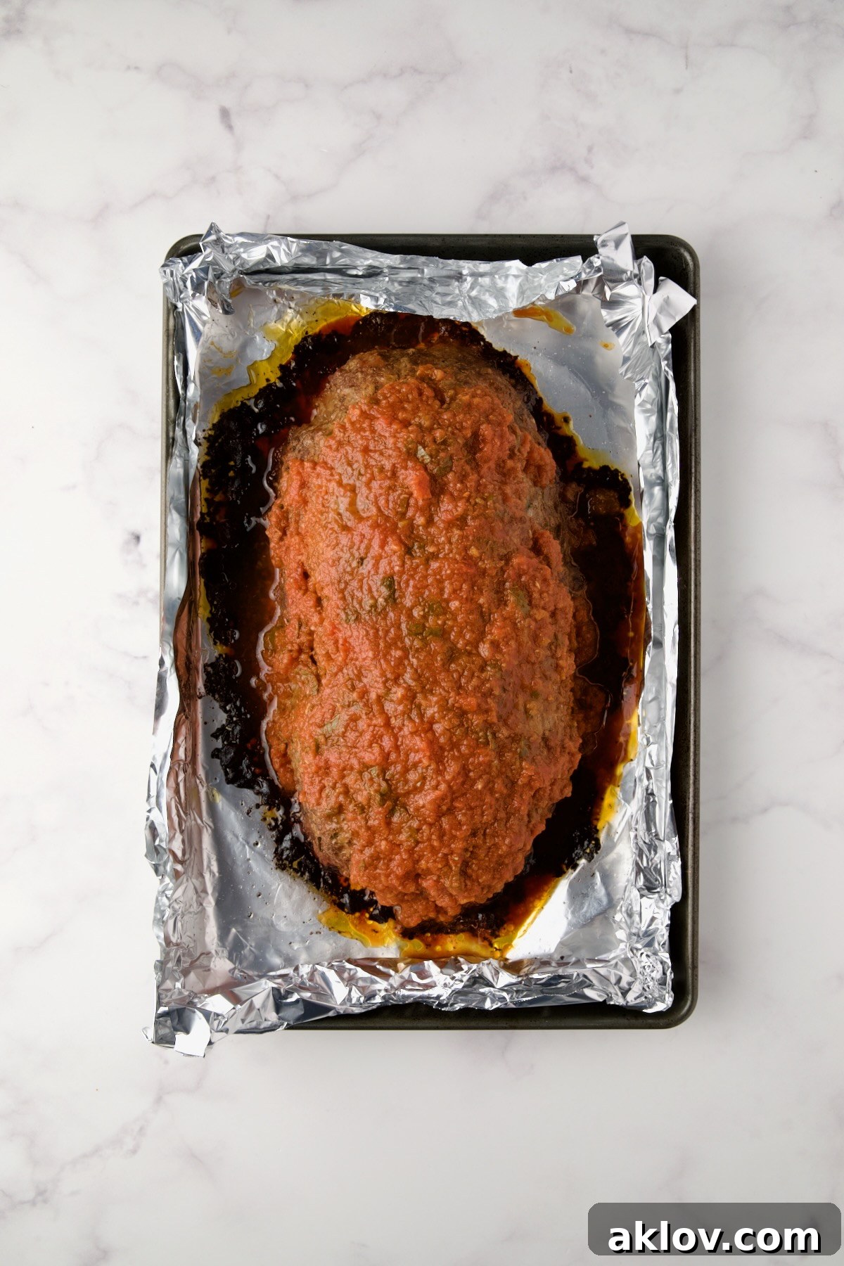 Baked meatloaf on an aluminum foil-lined sheet pan with marinara sauce added.