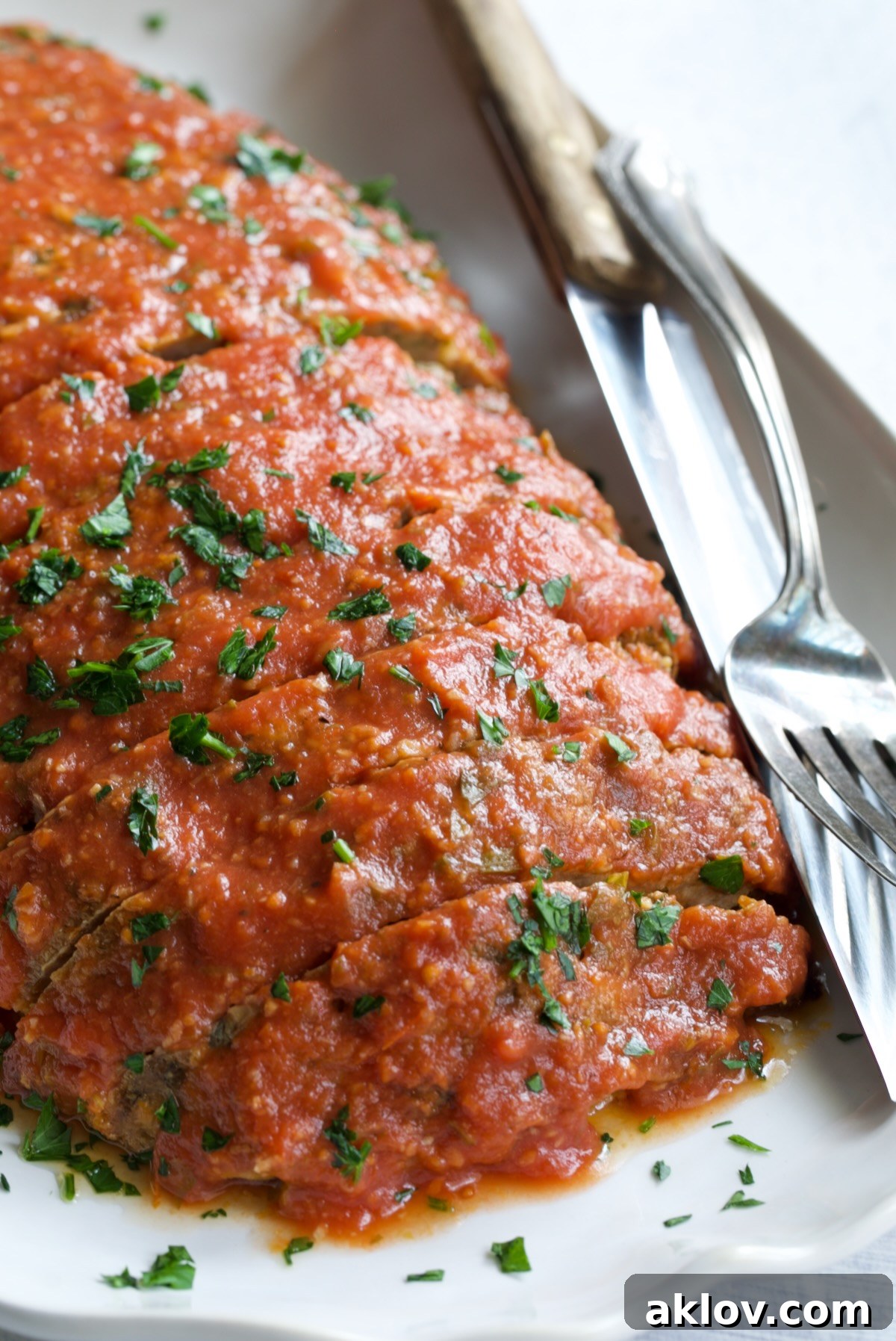 Italian Meatloaf on a white platter garnished with chopped fresh parsley.