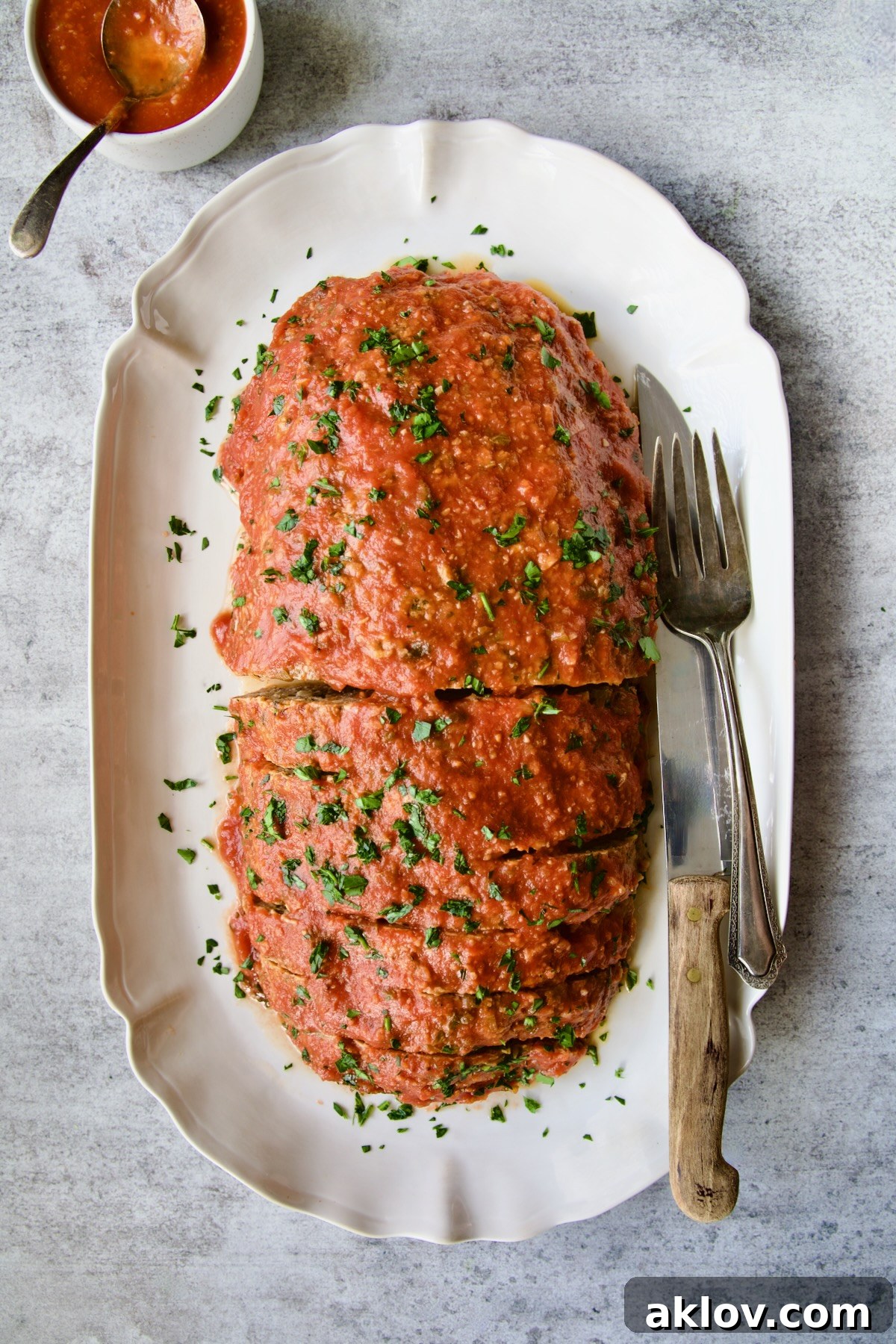 Italian Meatloaf on a white platter with serving utensils garnished with chopped fresh parsley.