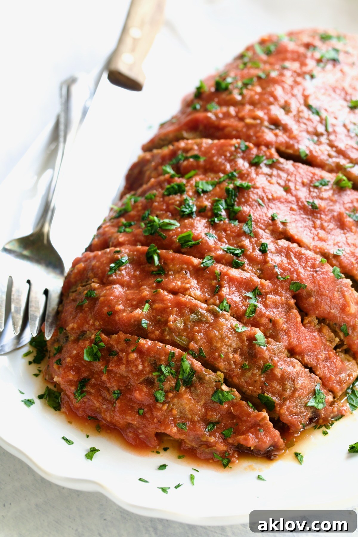 Italian Meatloaf on a white platter with serving utensils.