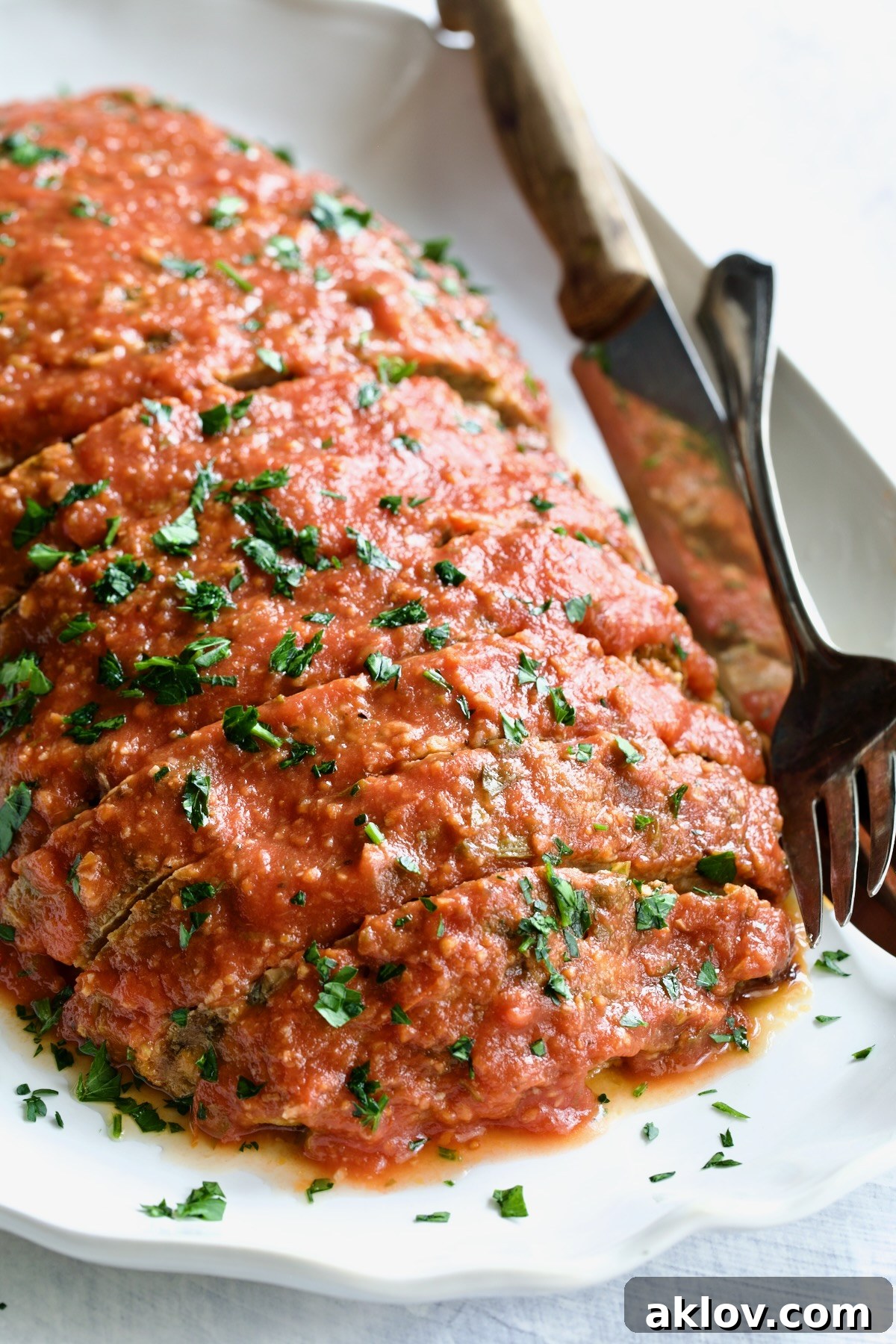 Italian Meatloaf on a white platter, garnished with fresh parsley, with serving utensils.