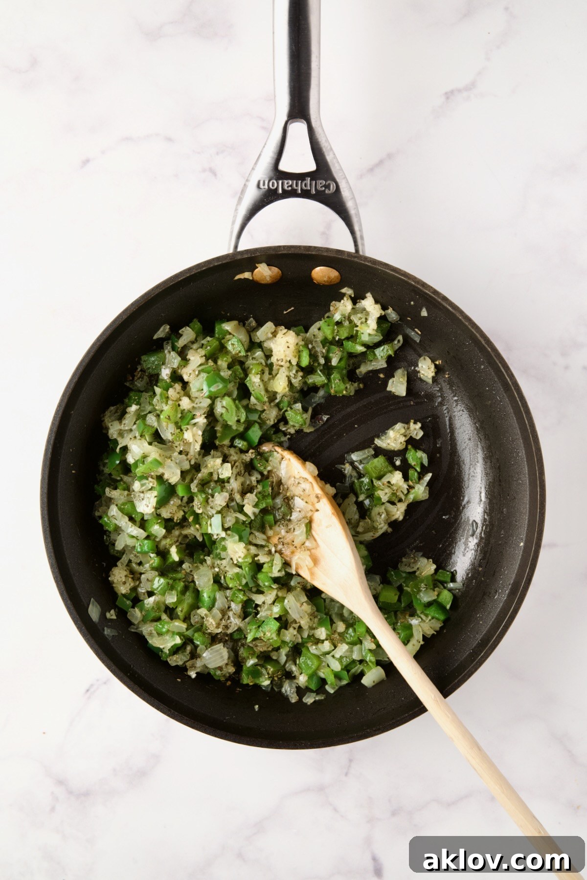 Cooked onions and green pepper in a nonstick skillet with a white spoon stirring in dried herbs and garlic.
