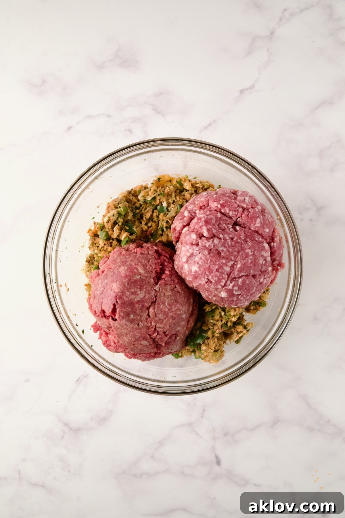 Ground meats added to other ingredients in a glass bowl.