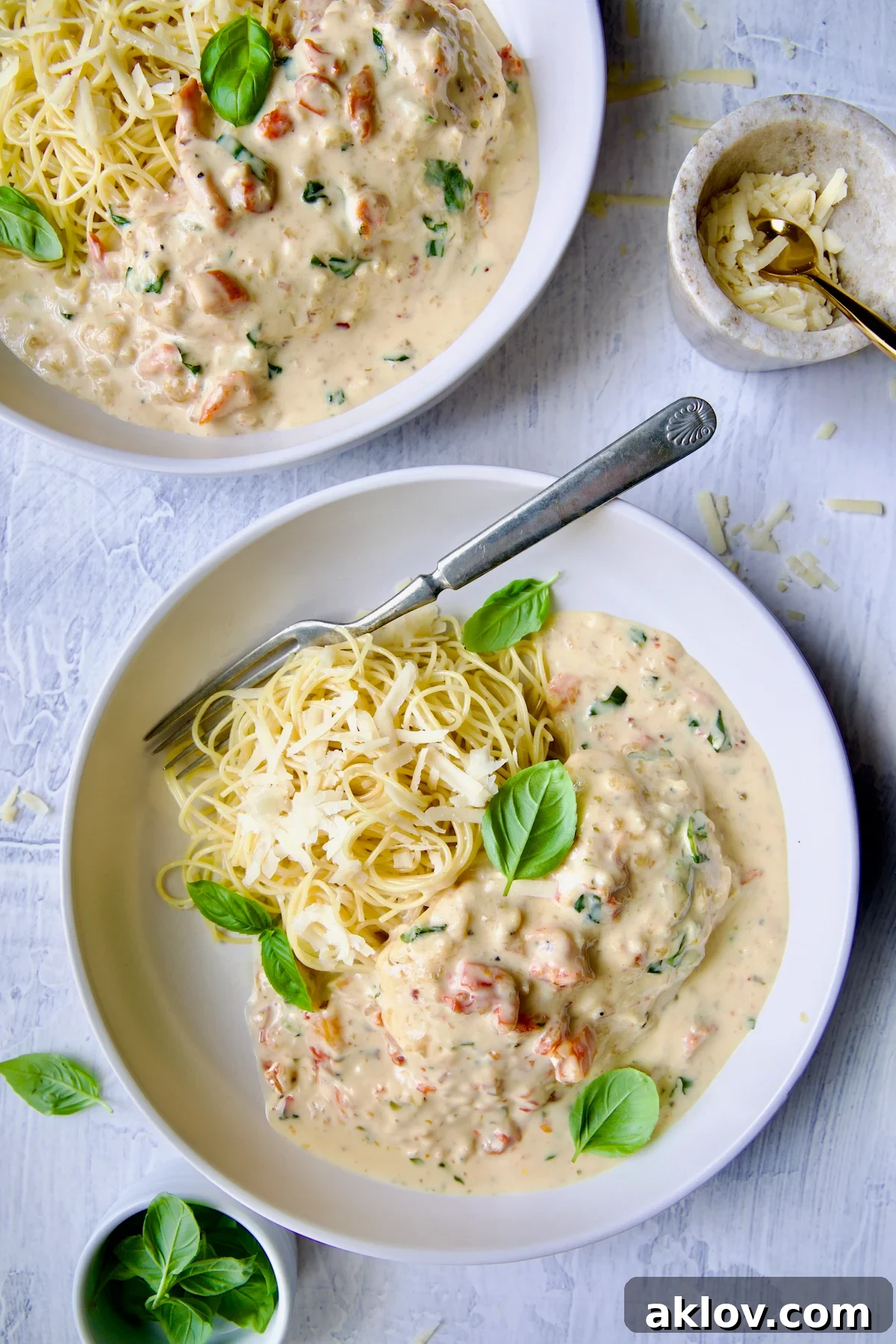 Marry Me Chicken in white bowl with angel hair pasta and fork garnished with fresh basil leaves.