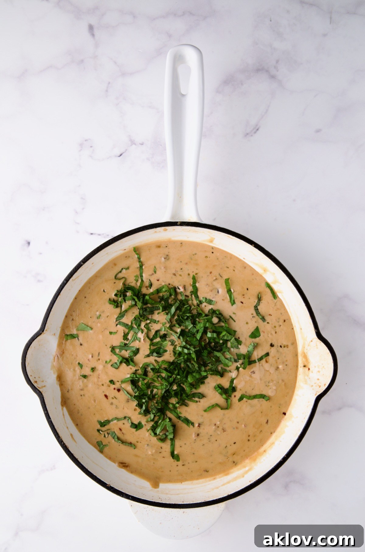 Finished sauce in white enamel cast iron skillet with fresh basil added.