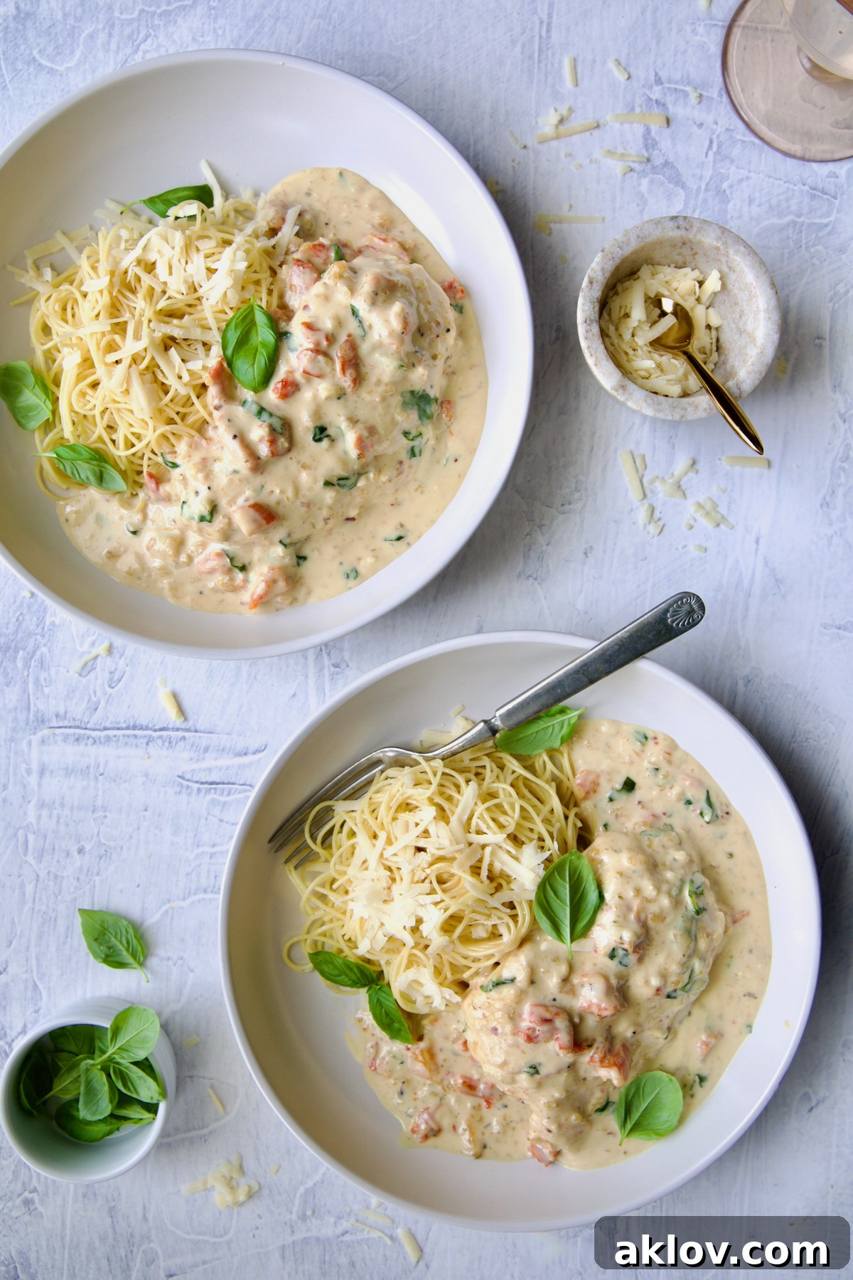 Two servings of Marry Me Chicken in white bowls with angel hair pasta and fork garnished with fresh basil leaves.