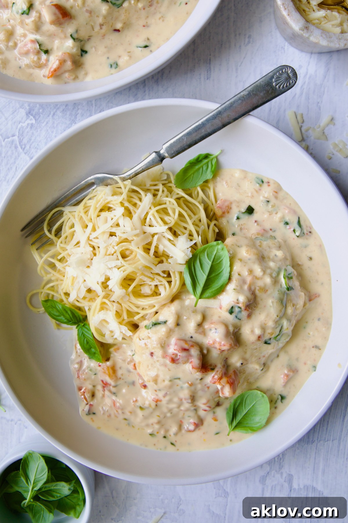 Marry Me Chicken in white bowl with angel hair pasta and fork garnished with fresh basil leaves.