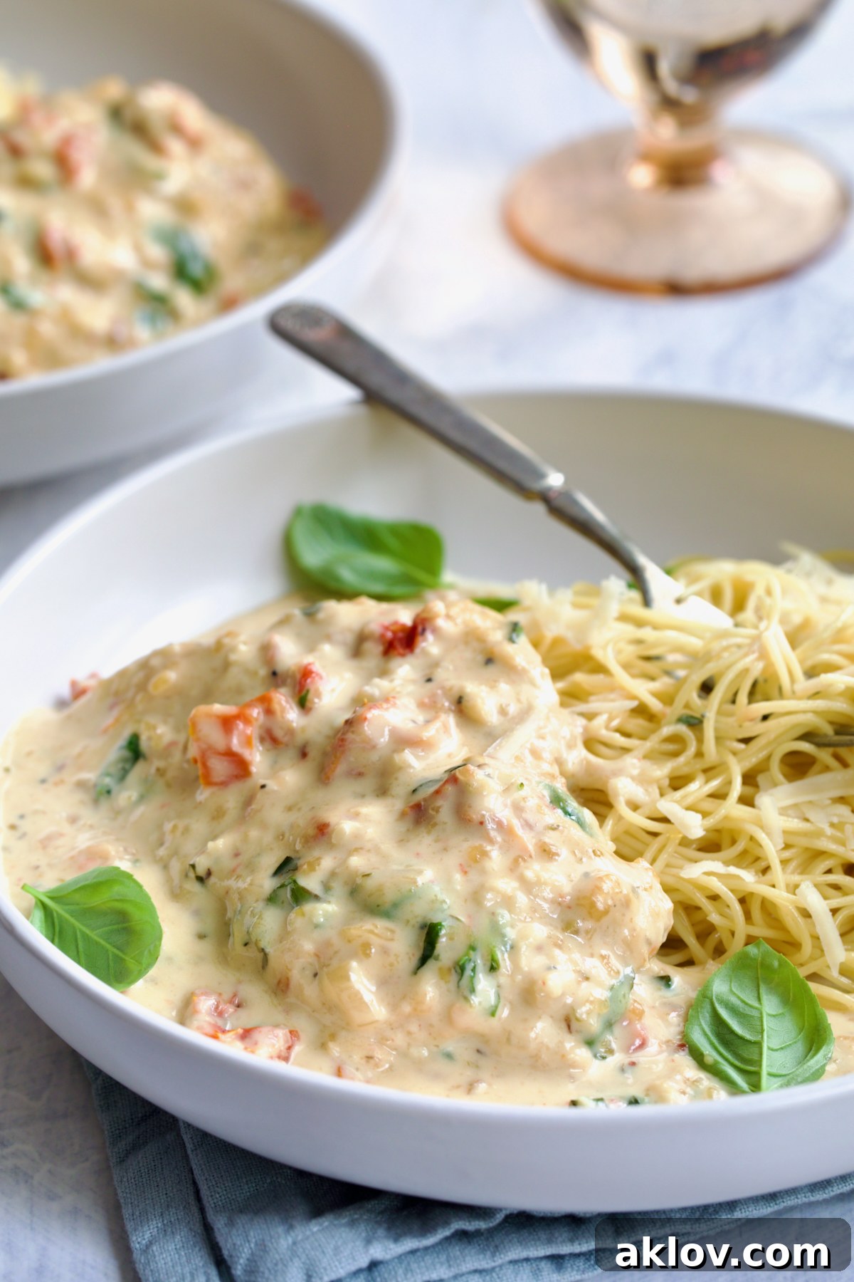 One serving of Marry Me Chicken in white bowl with angel hair pasta and fork garnished with fresh basil leaves.