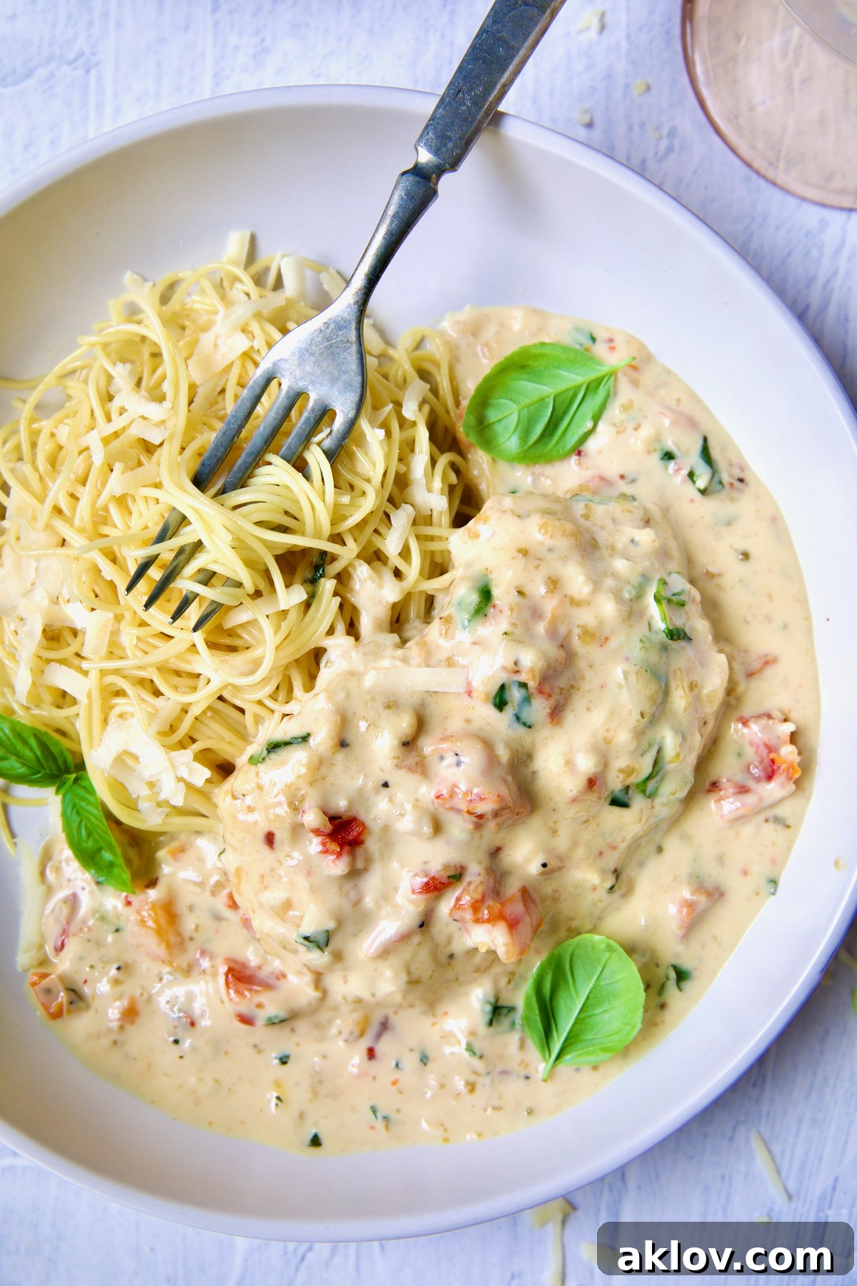 One serving of Marry Me Chicken in white bowl with angel hair pasta and fork garnished with fresh basil leaves.