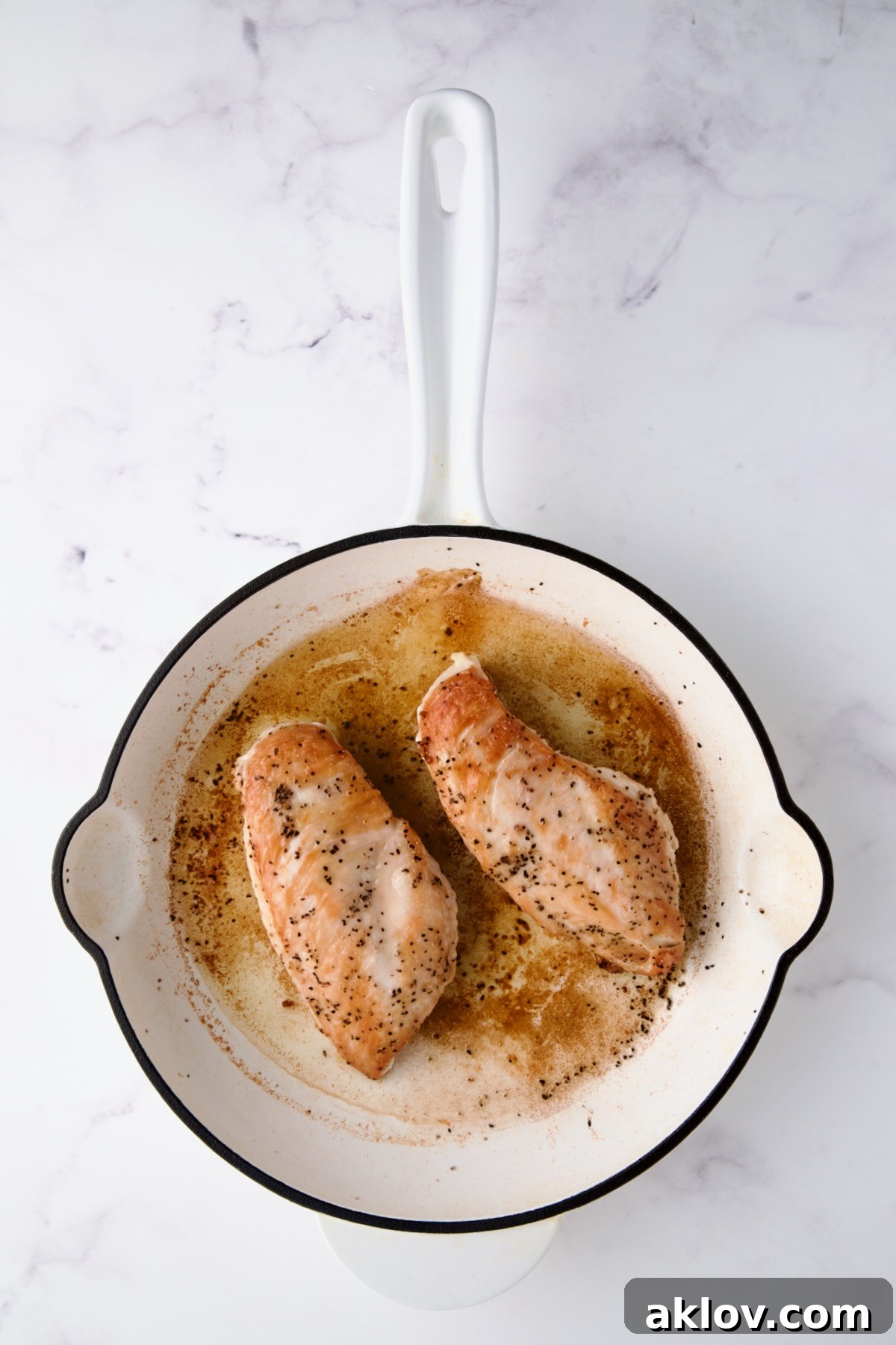 Two browned boneless skinless chicken breast halves in white enamel cast iron skillet.