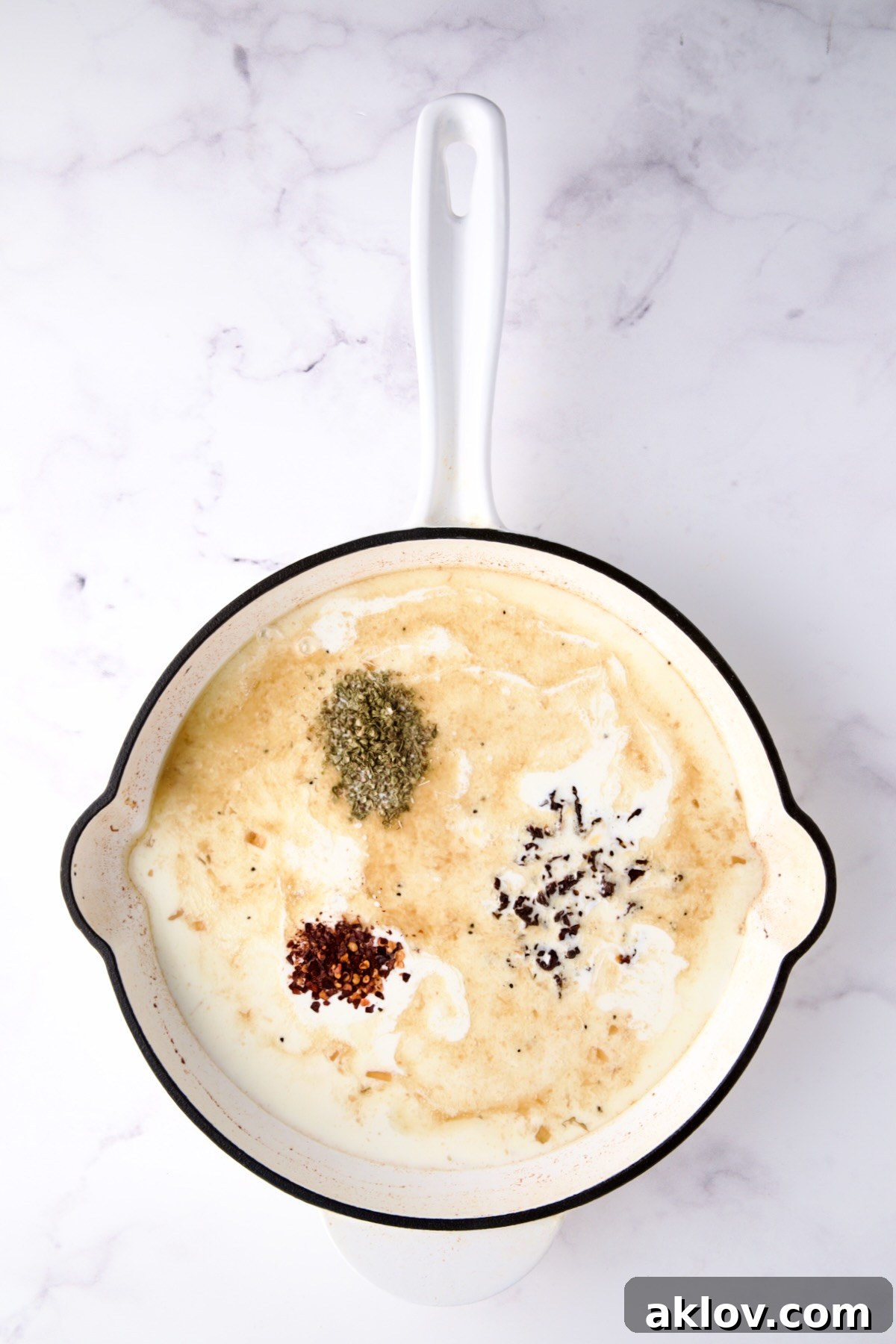 Chicken broth, heavy cream, sun dried tomatoes, dried oregano and red pepper flakes in white enamel cast iron skillet.