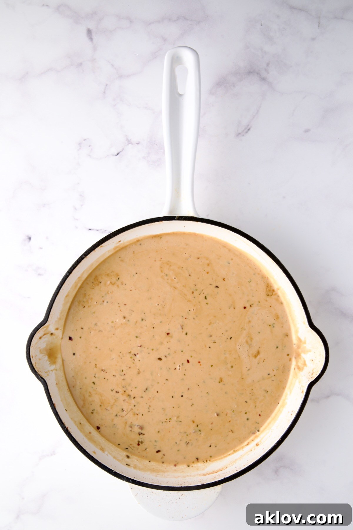 Finished cream sauce in white enamel cast iron skillet.