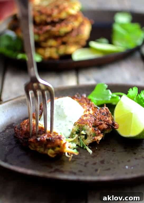 A freshly cooked zucchini fritter being pierced by a fork, highlighting its crispy texture.
