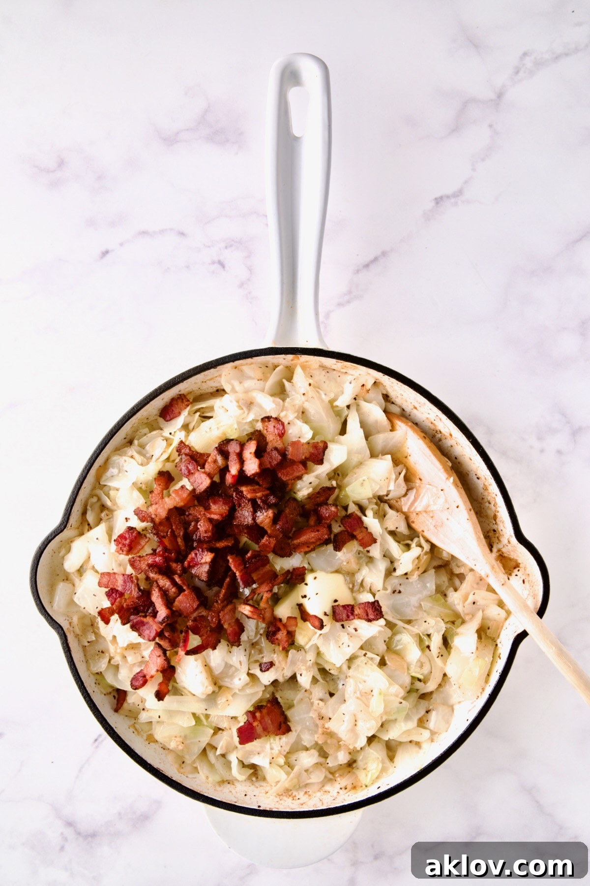 Bacon added back to cooked cabbage in white enamel cast iron skillet.