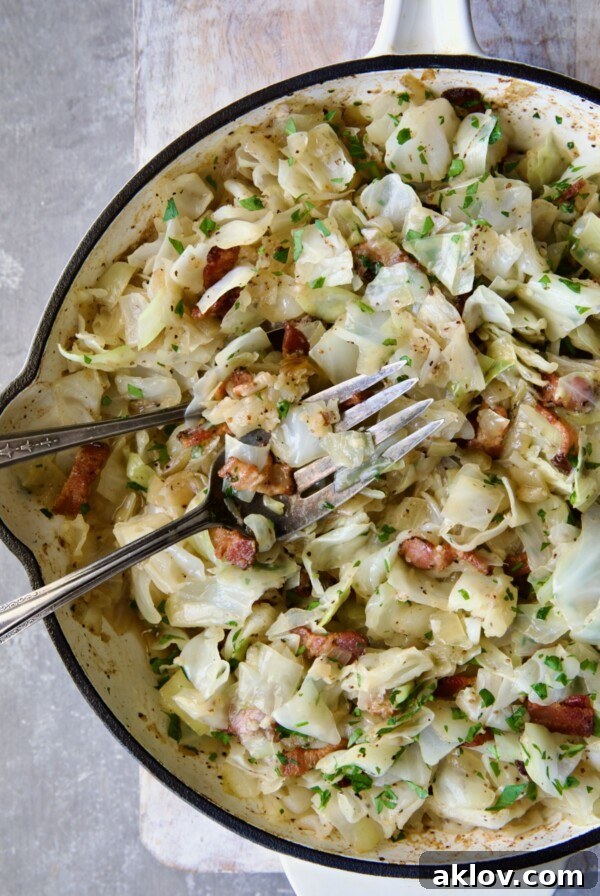 Two serving utensils serving up Fried Cabbage with Bacon from white enamel cast iron skillet.
