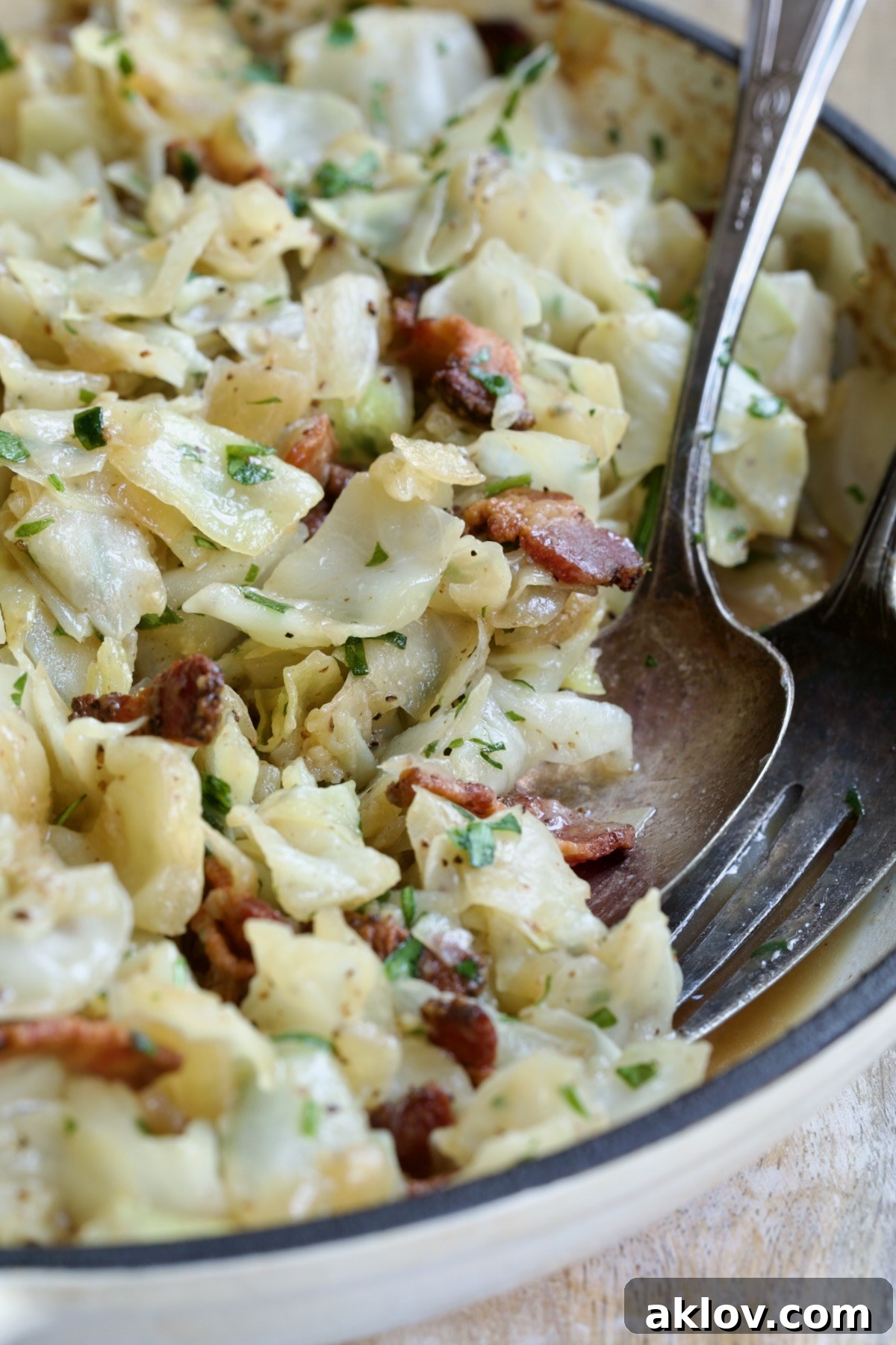 Two serving utensils serving up Fried Cabbage with Bacon.