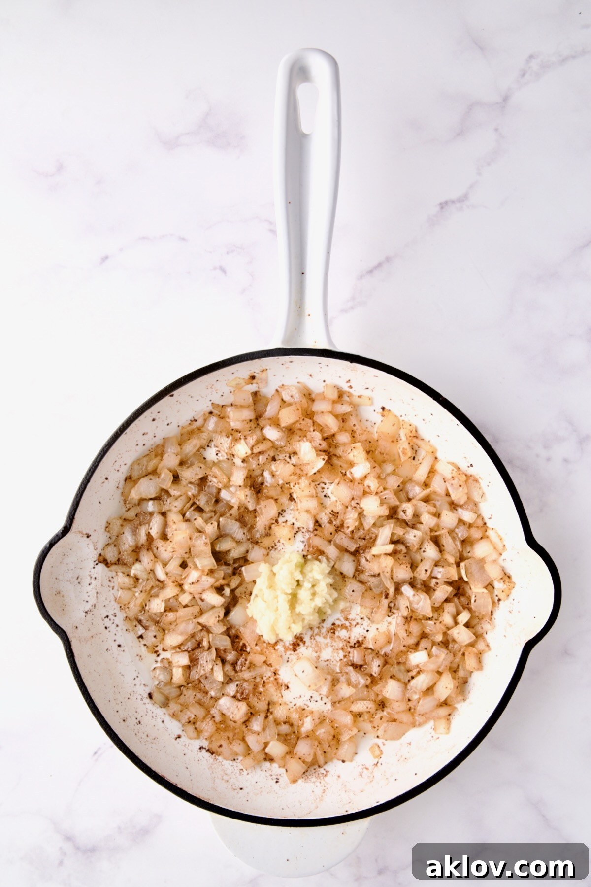 Cooked onions with fresh garlic added to white enamel cast iron skillet.