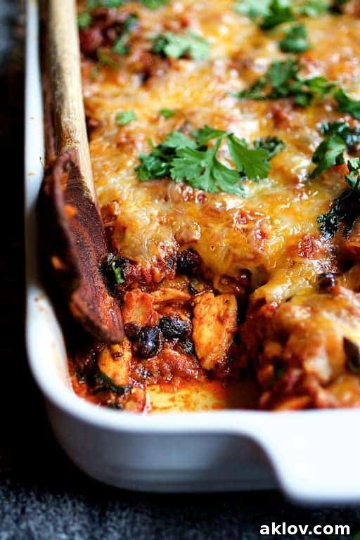 Mexican Chicken Tortilla Casserole in white baking dish with some removed, an easy and cheesy meal.