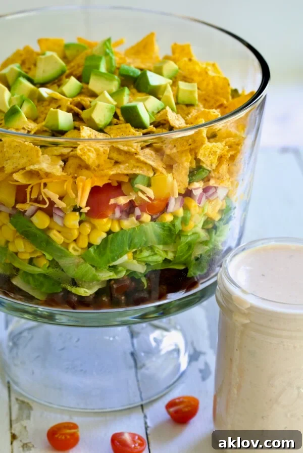 Southwestern Layered Salad in glass footed bowl with salad dressing in glass jar, a fun and updated twist on traditional layered salad.