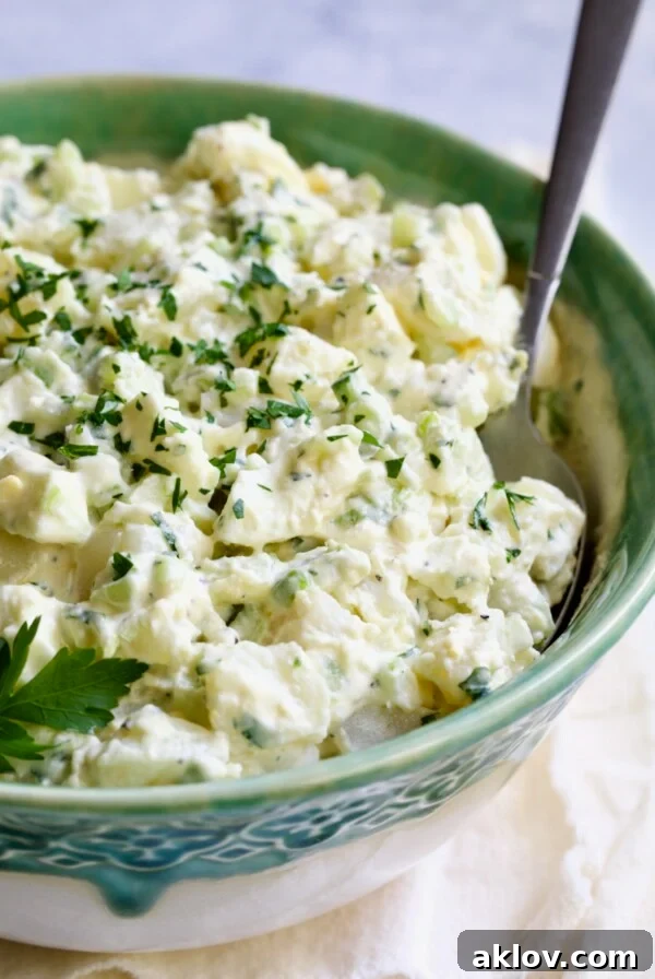 Creamy Potato Cucumber Salad in green and white serving bowl with serving spoon, an award-winning recipe.