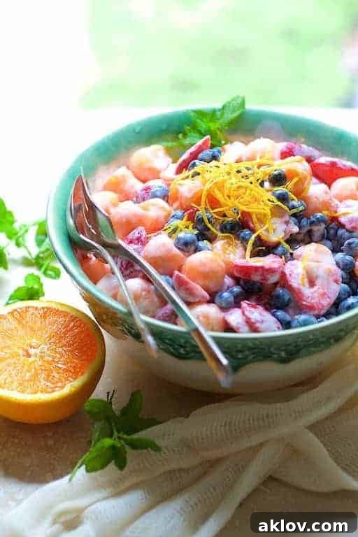 Summer Fruit Salad with Orange Yogurt Vanilla Dressing in green decorative bowl garnished with orange zest, a modern spin on a classic.