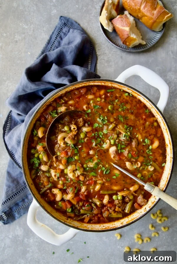 Hamburger Vegetable Soup in white Dutch oven with soup ladle, a hearty and comforting meal for fall and winter.