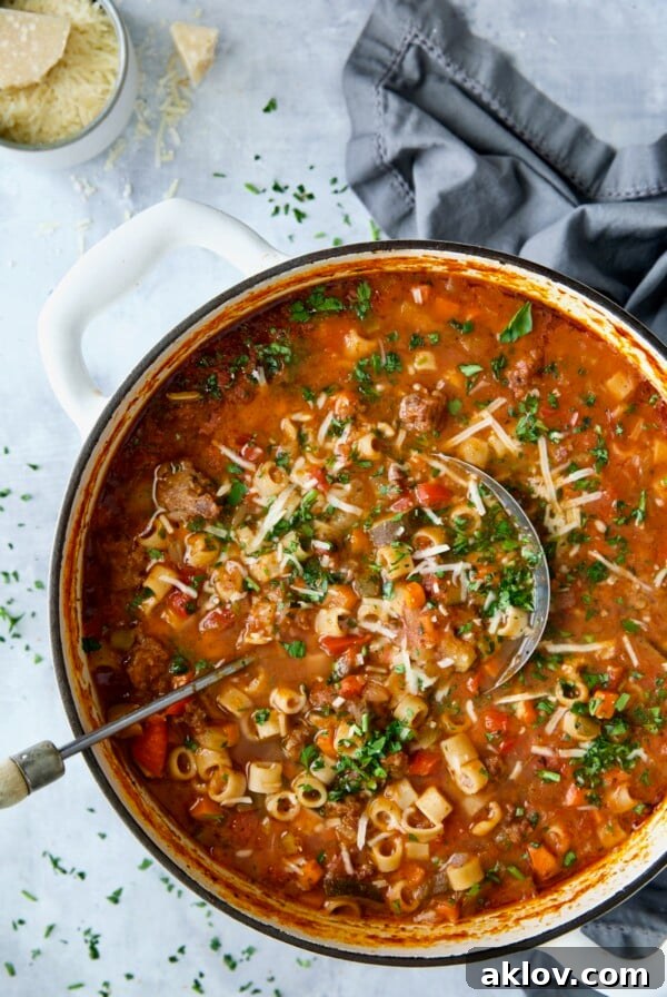 Italian Sausage Soup in white Dutch oven garnished with fresh parsley and Parmesan cheese, a soul-satisfying meal.