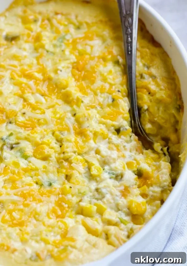 Cream Cheese Corn Casserole with Green Chiles in white oval baking dish with serving spoon, an easy and decadent family favorite.