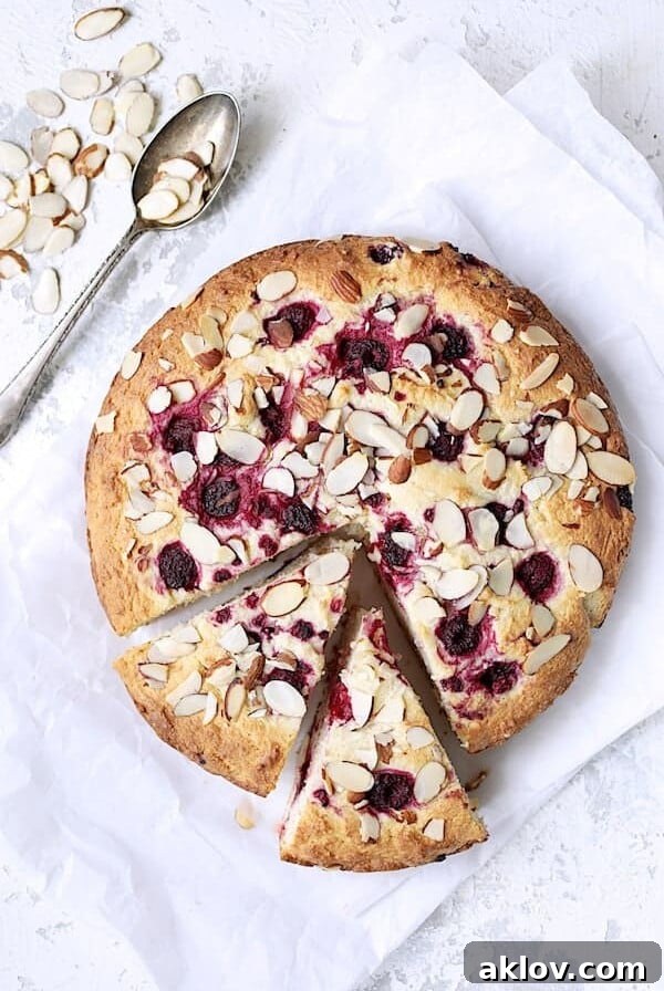 Raspberry Ricotta Cake with Almonds - Overhead hero shot of cake on white paper with two pieces cut into it and almonds scattered about, moist, fluffy, and super easy to make.