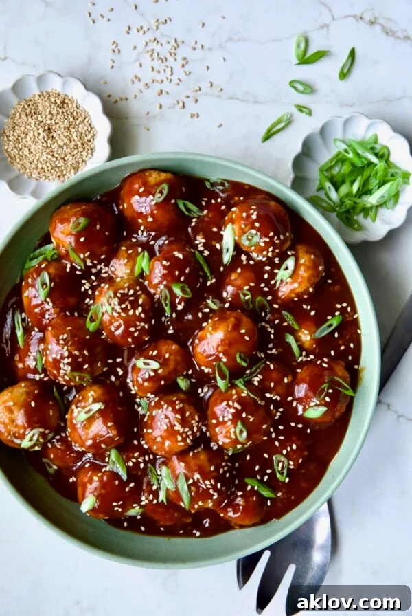 Asian Chicken Meatballs in round green bowl garnished with sesame seeds and scallions, perfect as an appetizer or main course.