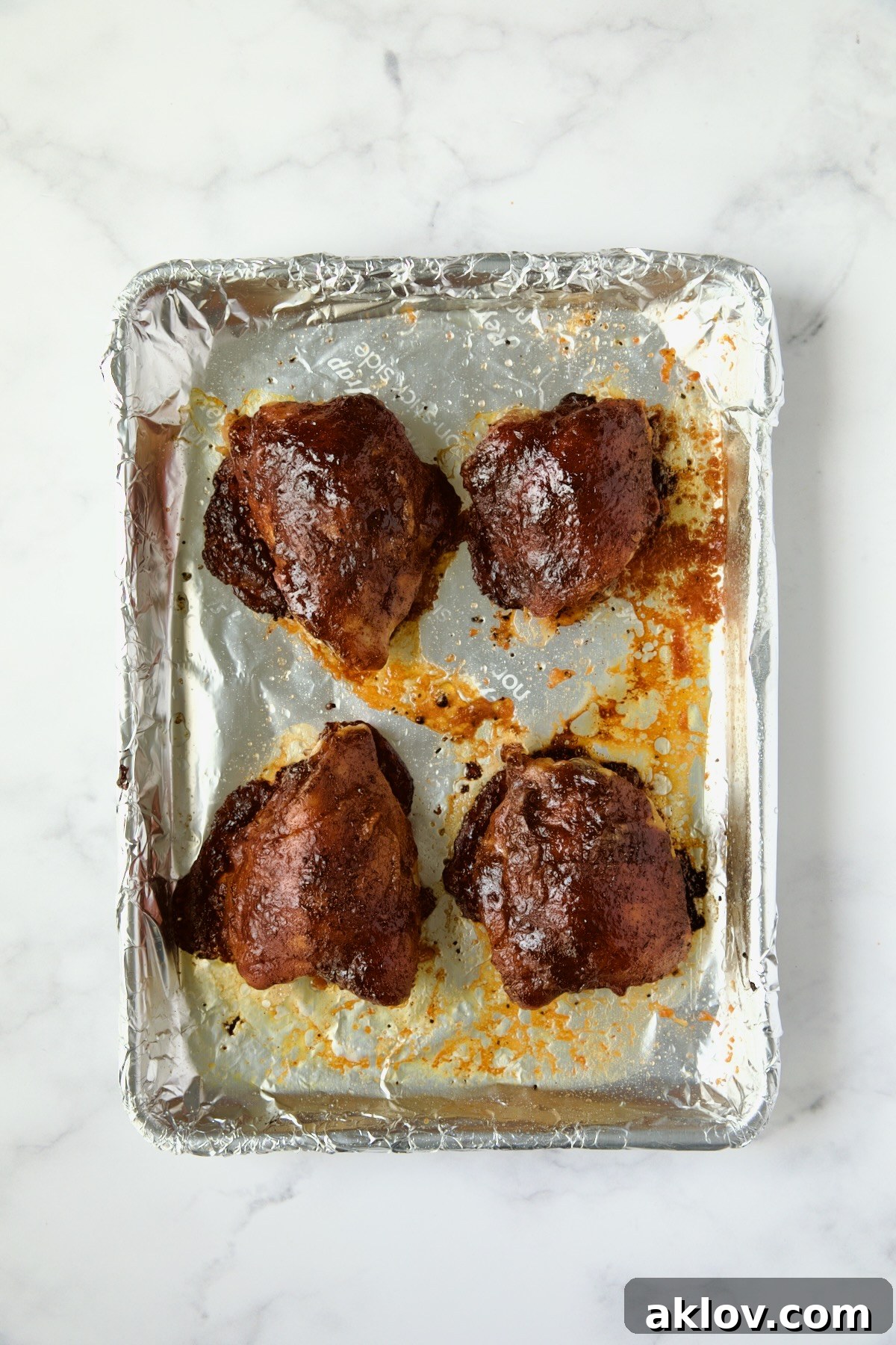 Four finished barbecue chicken thighs on aluminum foil-lined pan.