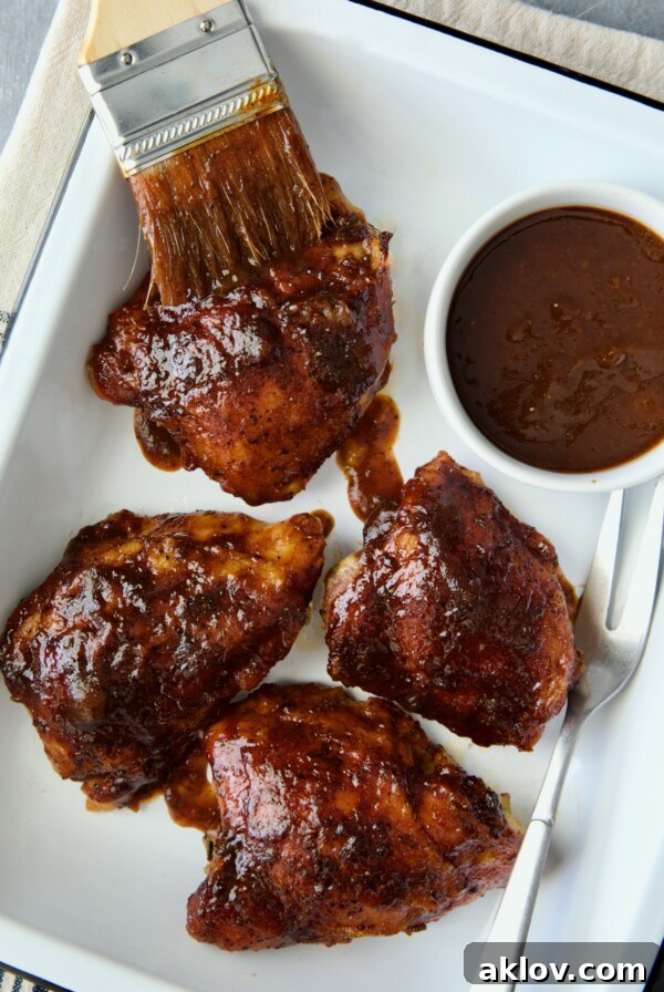 Four Baked BBQ Chicken Thighs in white enamel serving tray with bowl of barbecue sauce.