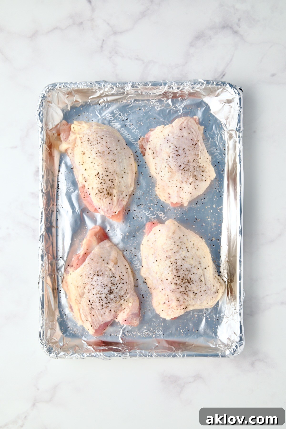 Four uncooked chicken thighs on aluminum foil-lined baking sheet.